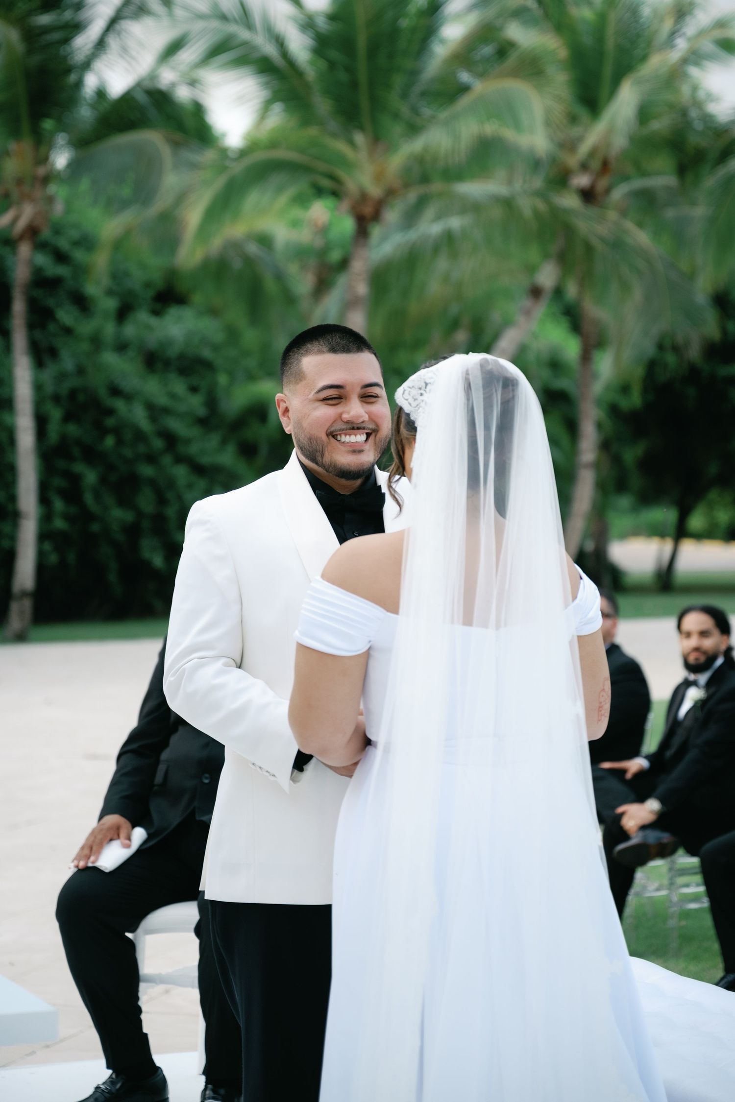Wedding guests gathered outdoors under palm trees during a tropical celebration.
