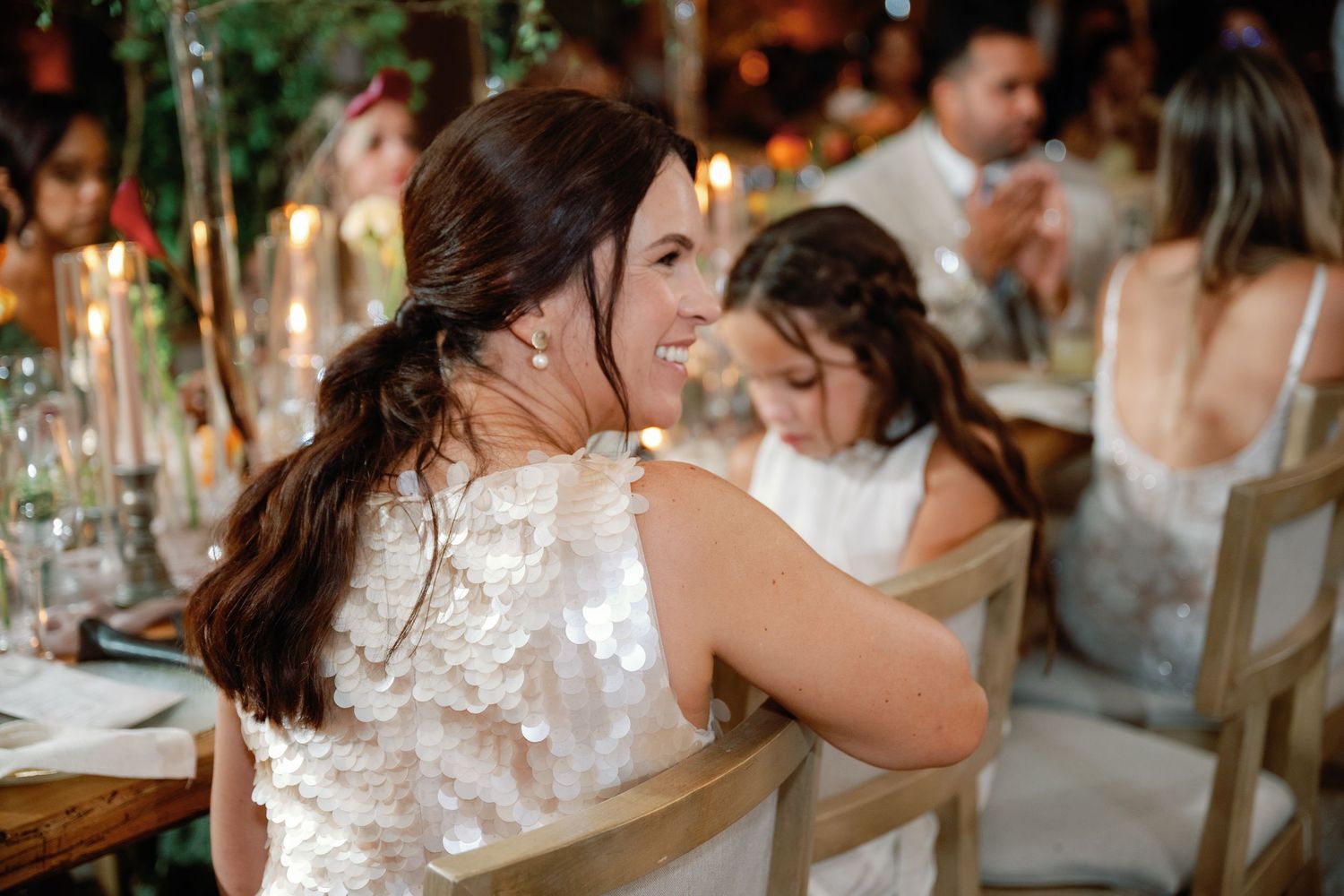 A group of people dance and celebrate together at a rustic wedding reception venue with string lights overhead.