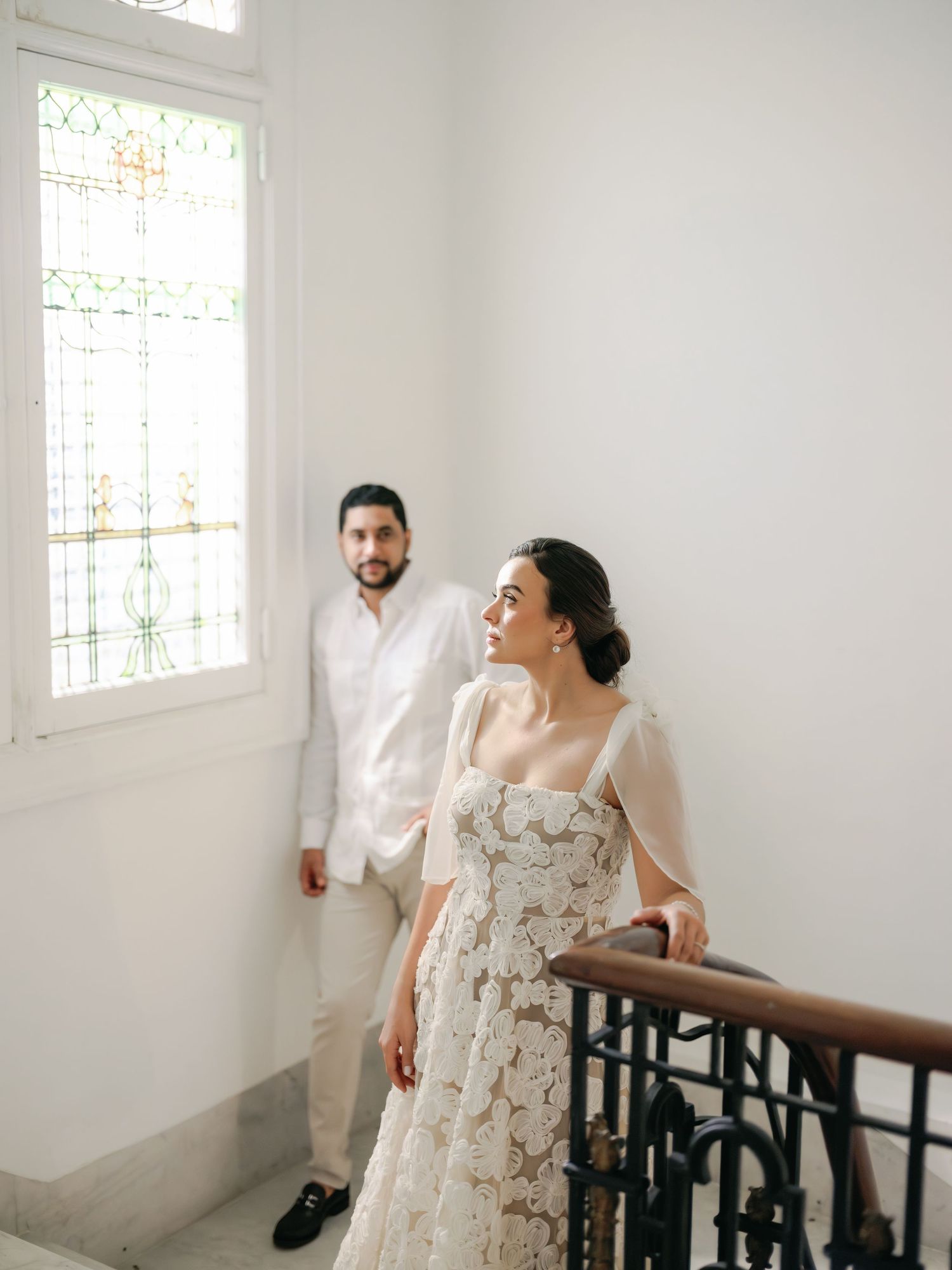 A couple shares a joyful moment on an elegant white staircase in formal wedding attire.