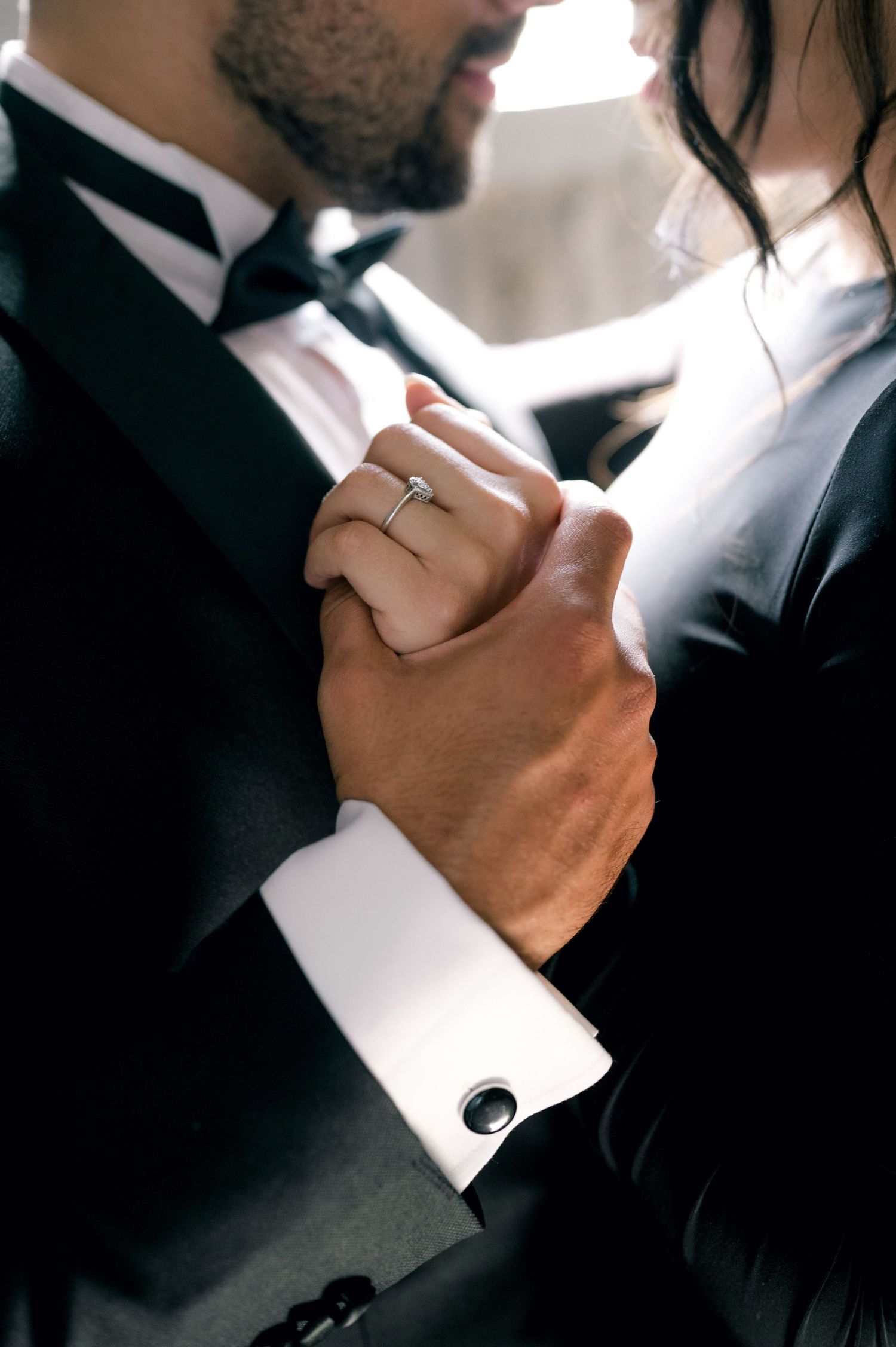 Close-up view of hands adjusting formal black suit cufflinks against white dress shirt sleeve.