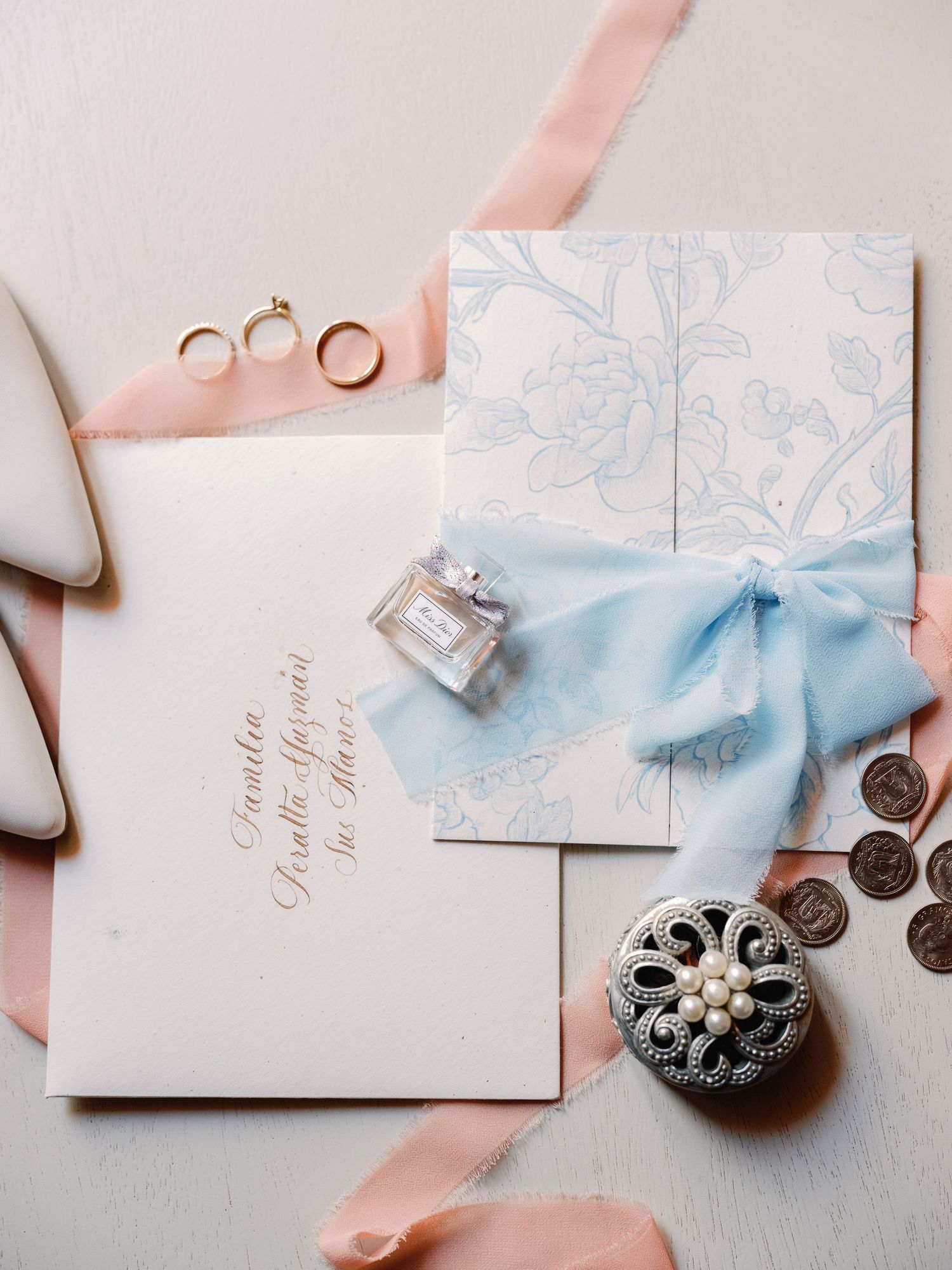 Wedding invitation suite in soft blue and blush tones with delicate ribbons and vintage-style buttons.