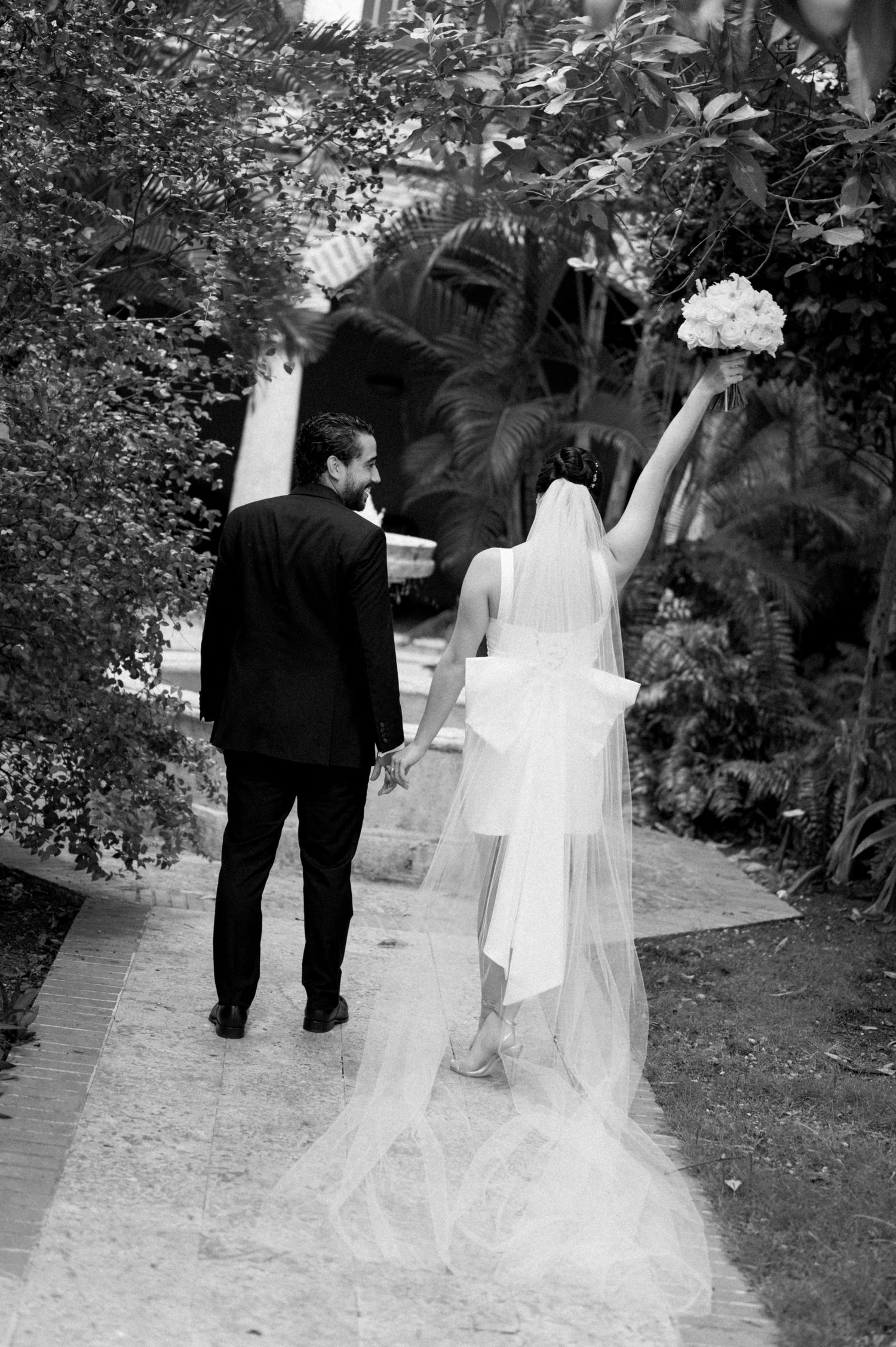A couple in wedding attire walks along a garden path in a series of black and white photos showing their progression.