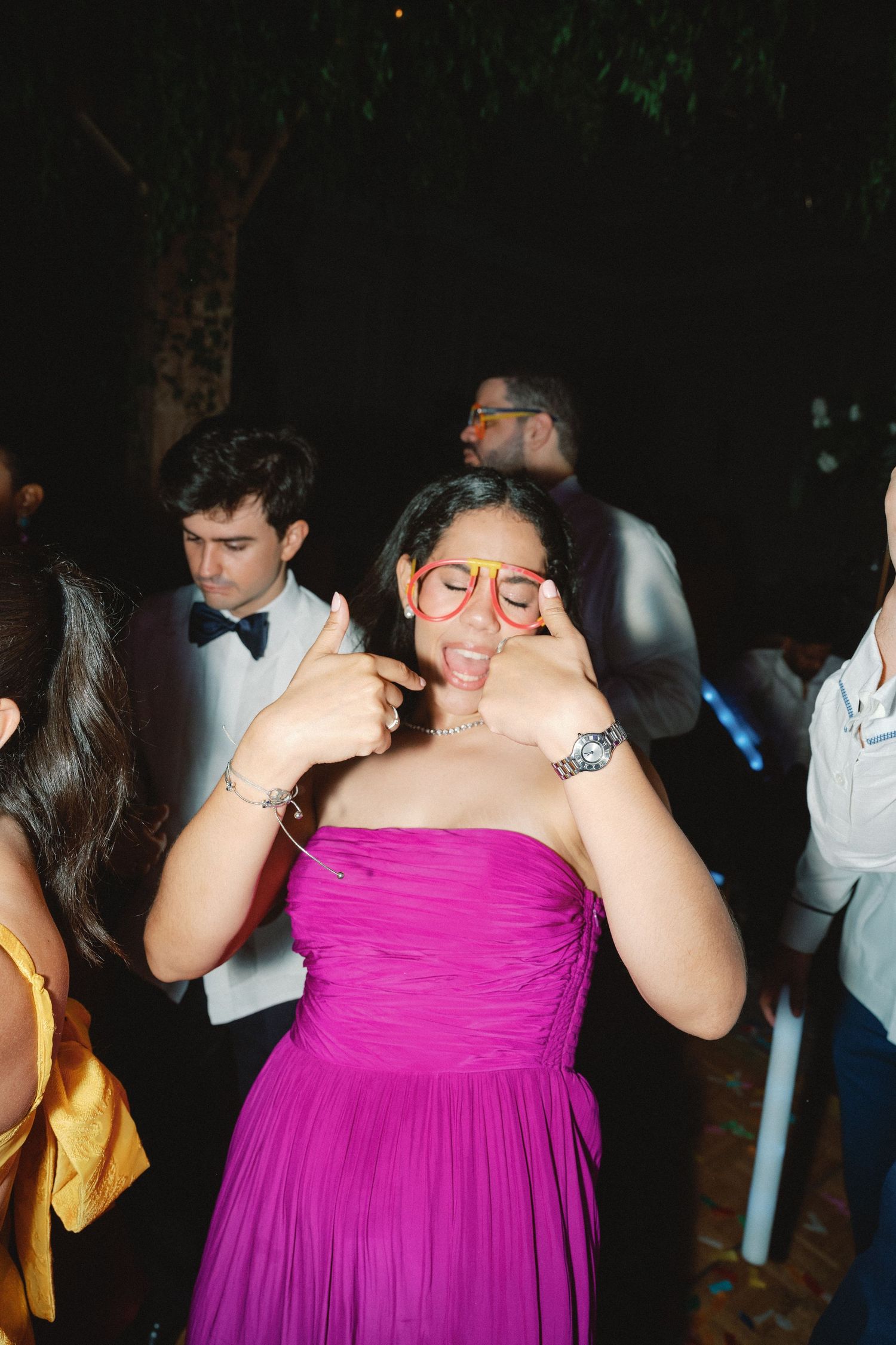 People dancing at a nighttime celebration wearing formal attire including bright pink dresses.