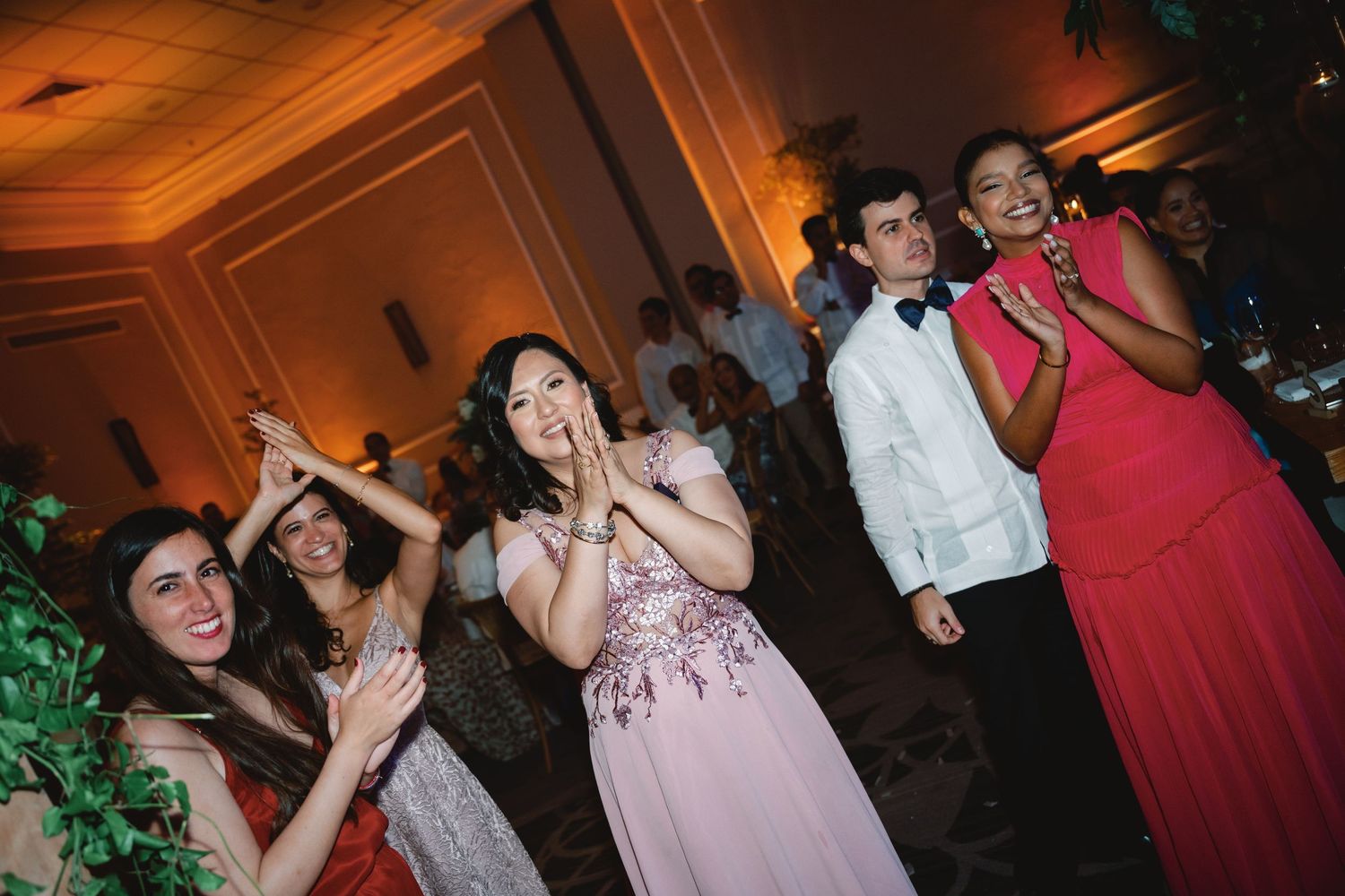 Wedding reception guests dance and celebrate on a warmly lit dance floor with decorative lighting.