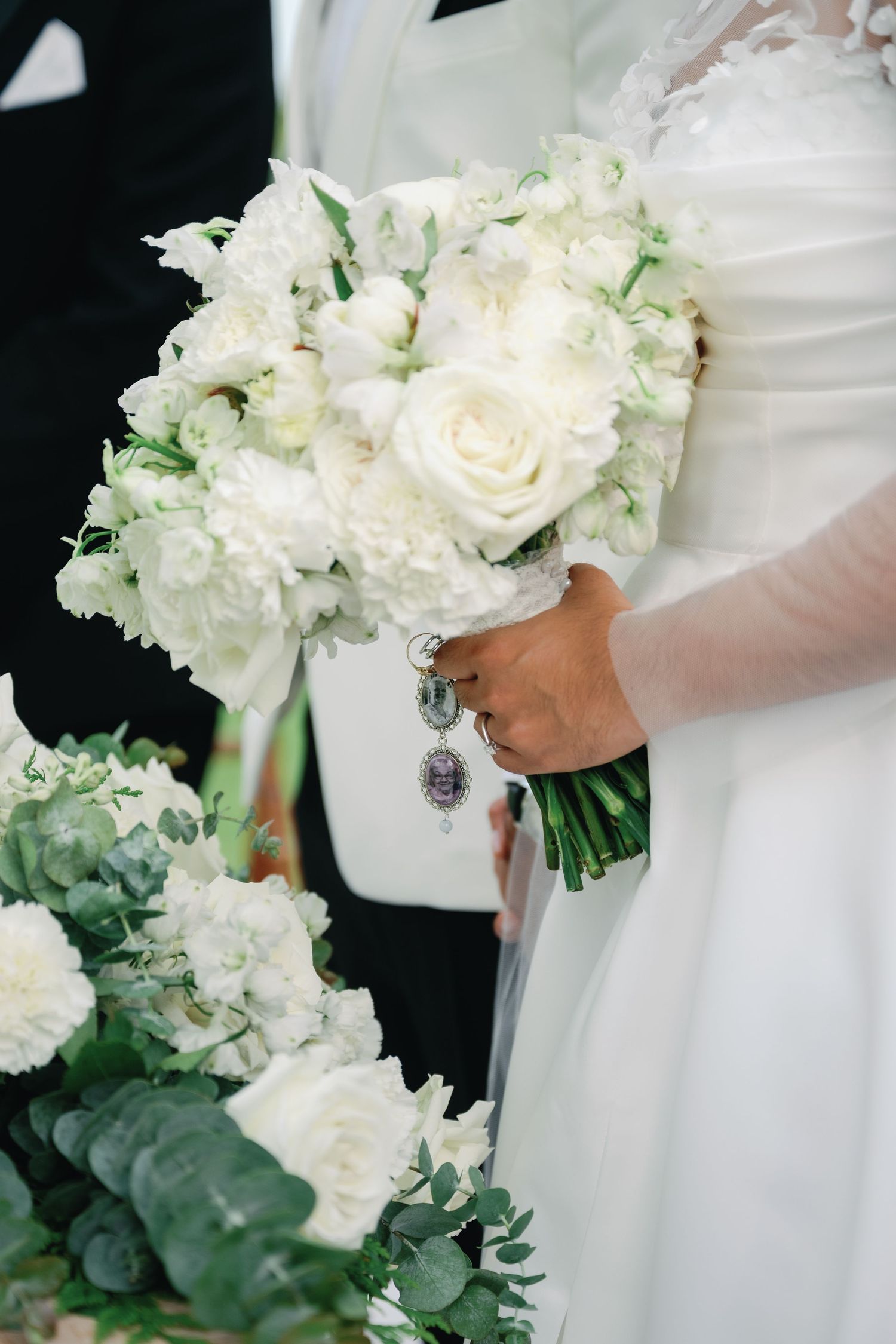 Elegant white wedding bouquets with roses and greenery held against white dresses in a formal setting.