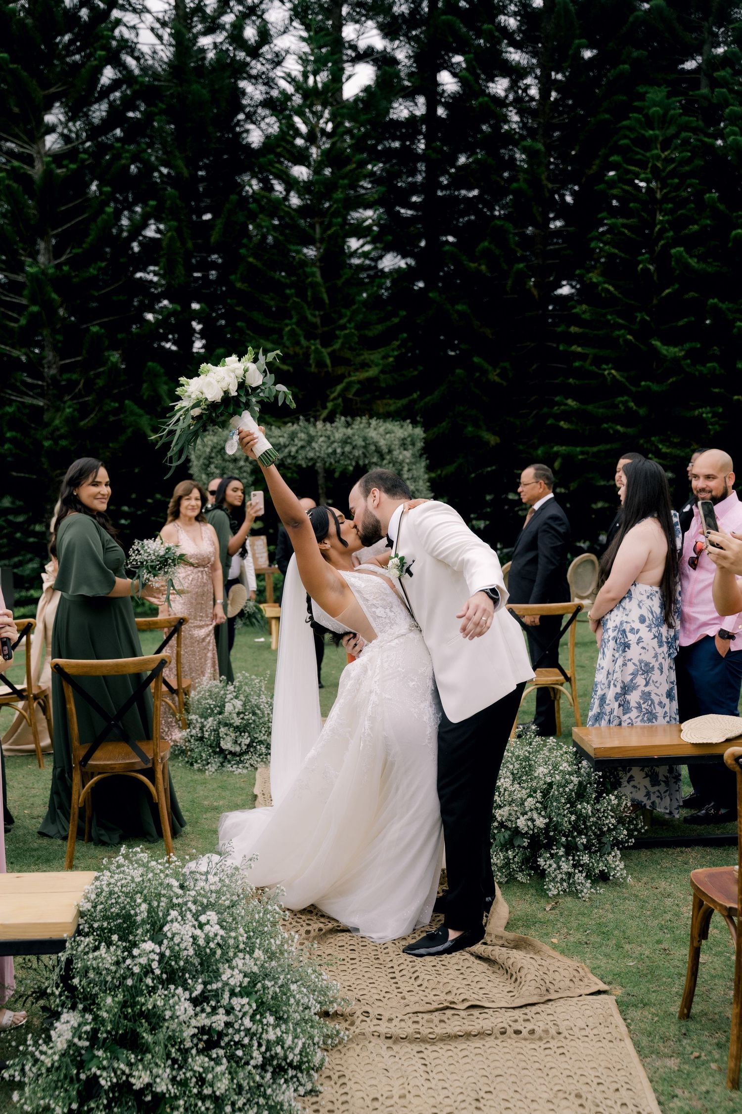 Wedding guests dancing and celebrating on an outdoor dance floor decorated with baby's breath flowers and wooden chairs.