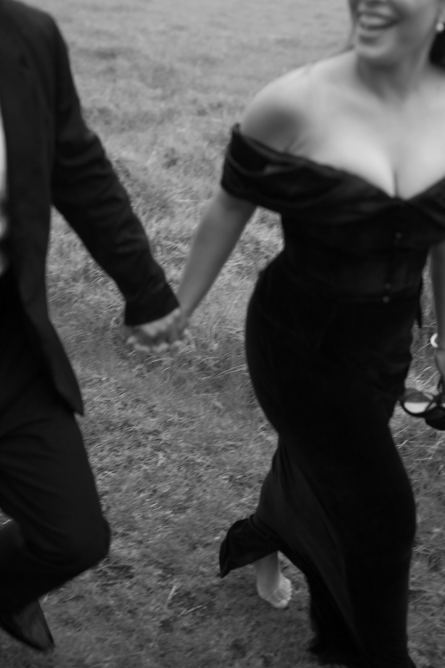 A couple holding hands while walking, with the person on right wearing an elegant black off-shoulder dress.