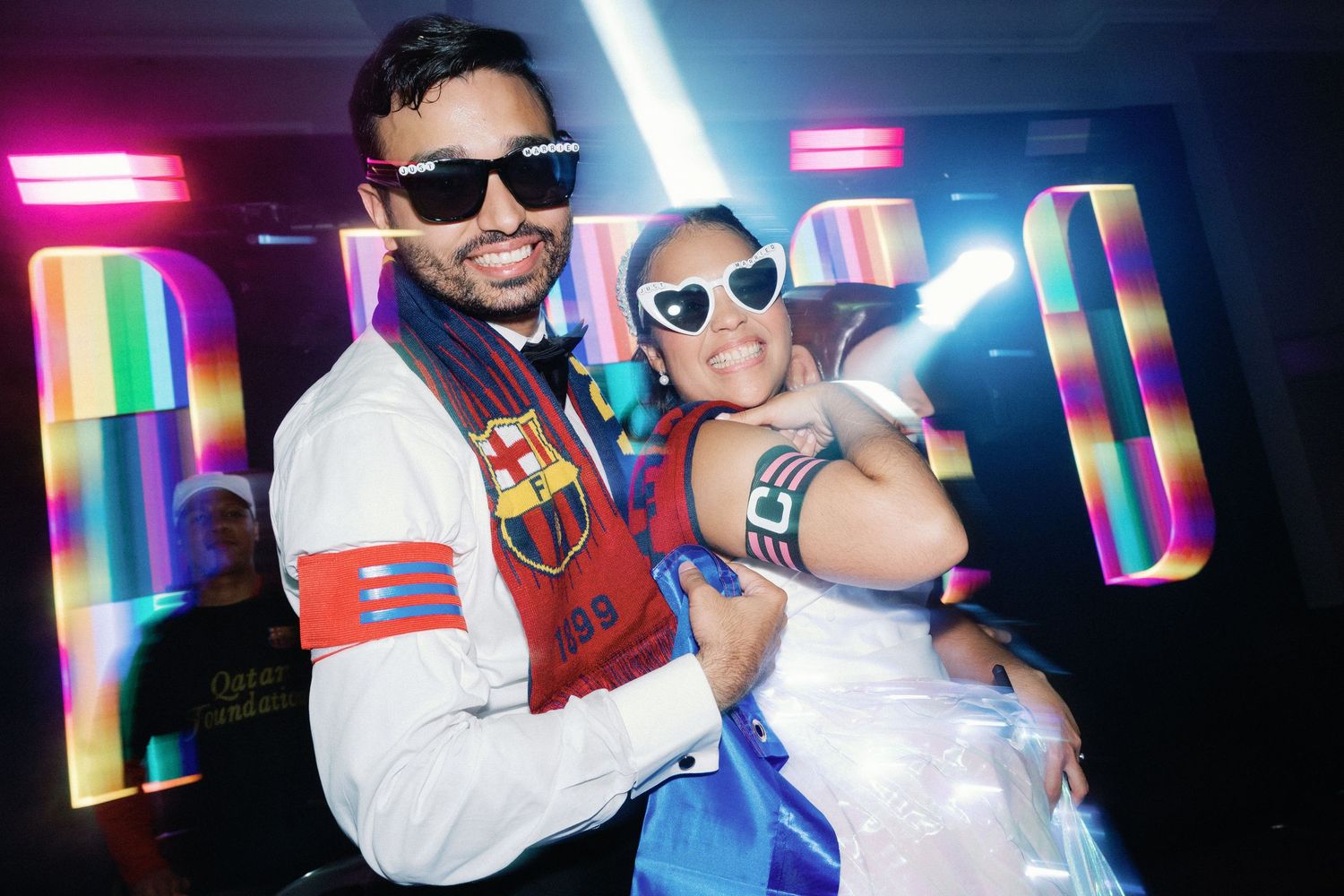 People posing in a colorful nightclub setting with neon lights and sunglasses.
