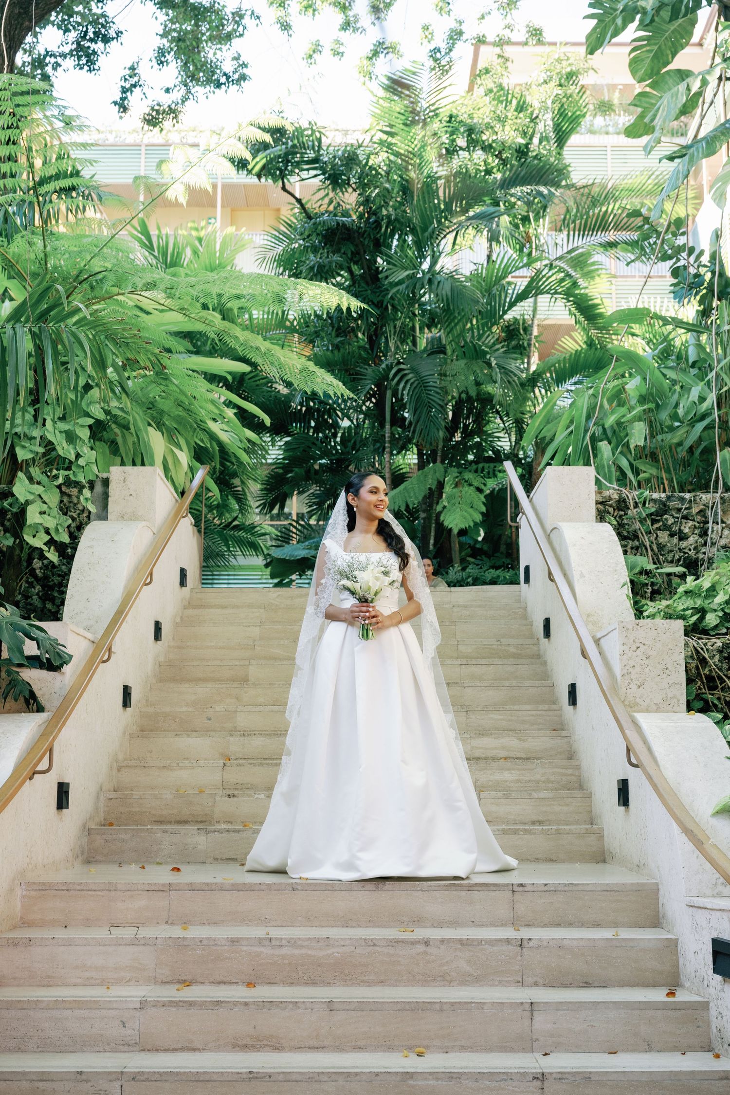 A sequence of photos showing a person in a white wedding gown descending elegant stone steps surrounded by lush greenery.