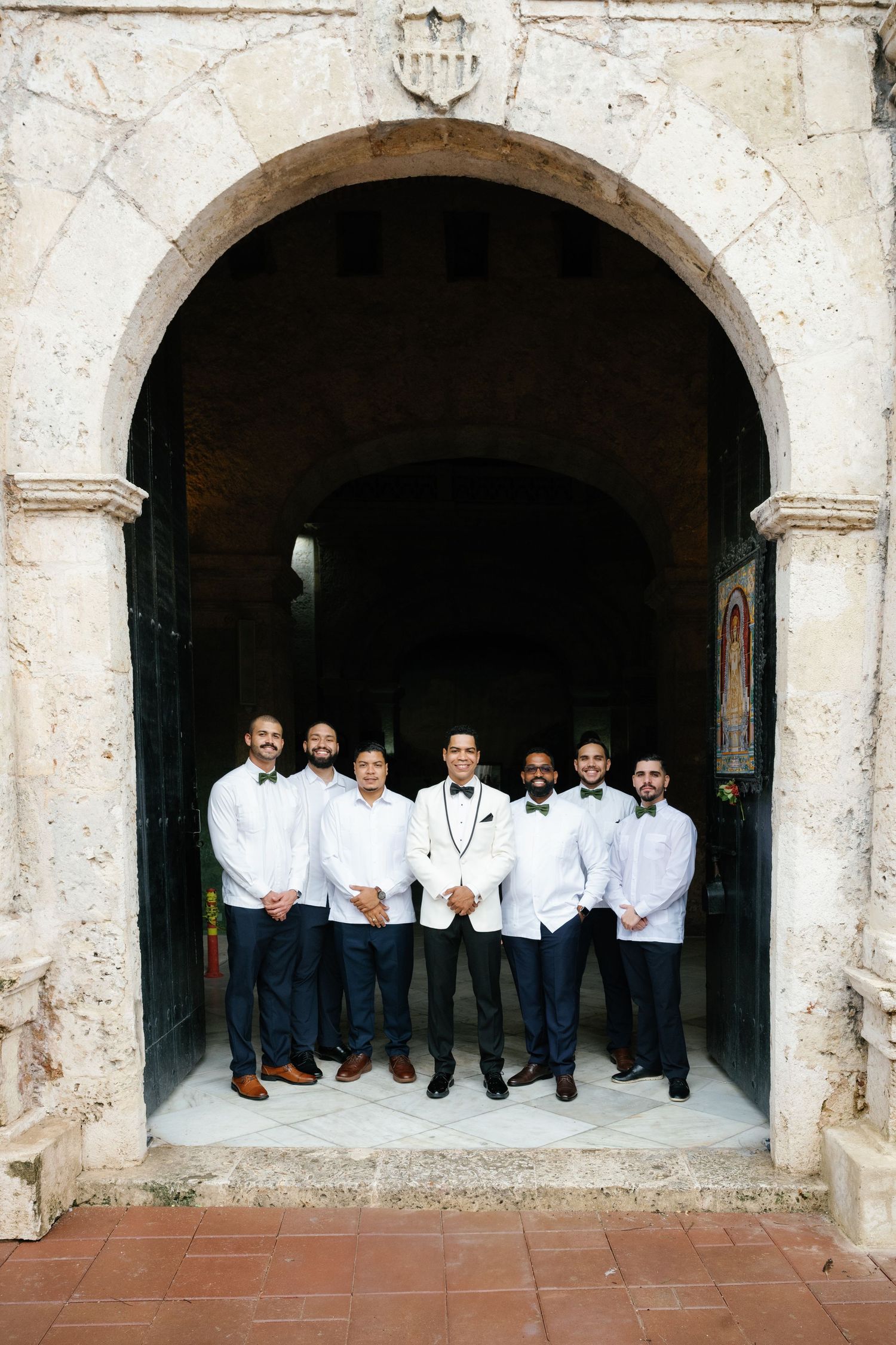 Groomsmen in white shirts pose together under stone archways at a historic venue.