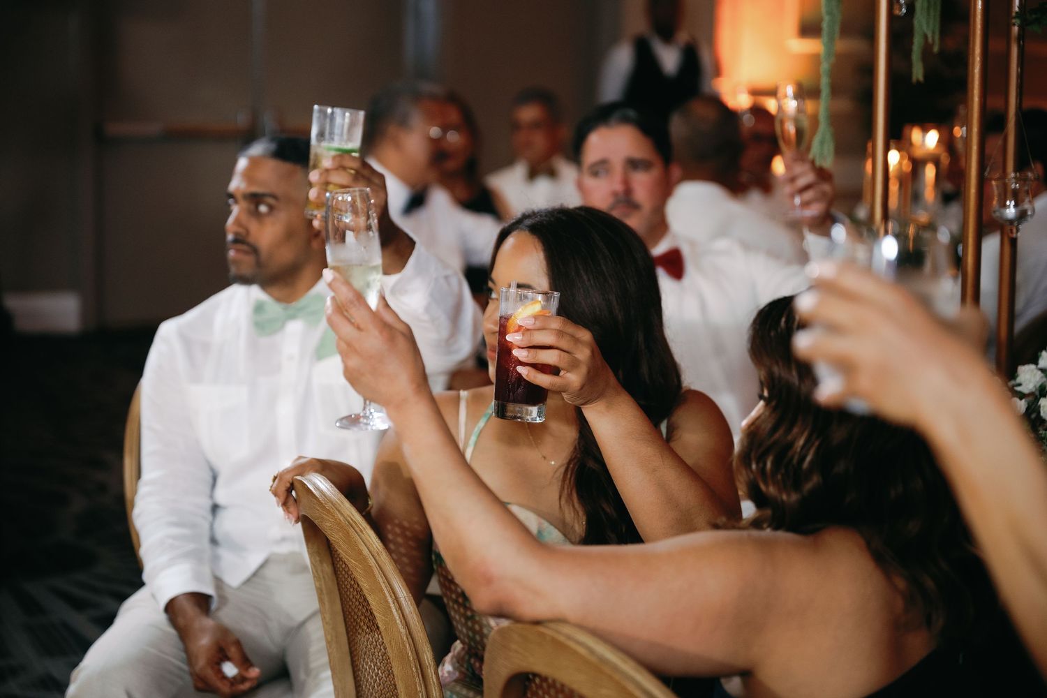 Wedding reception guests raise their drinks in celebration during a festive toast moment.