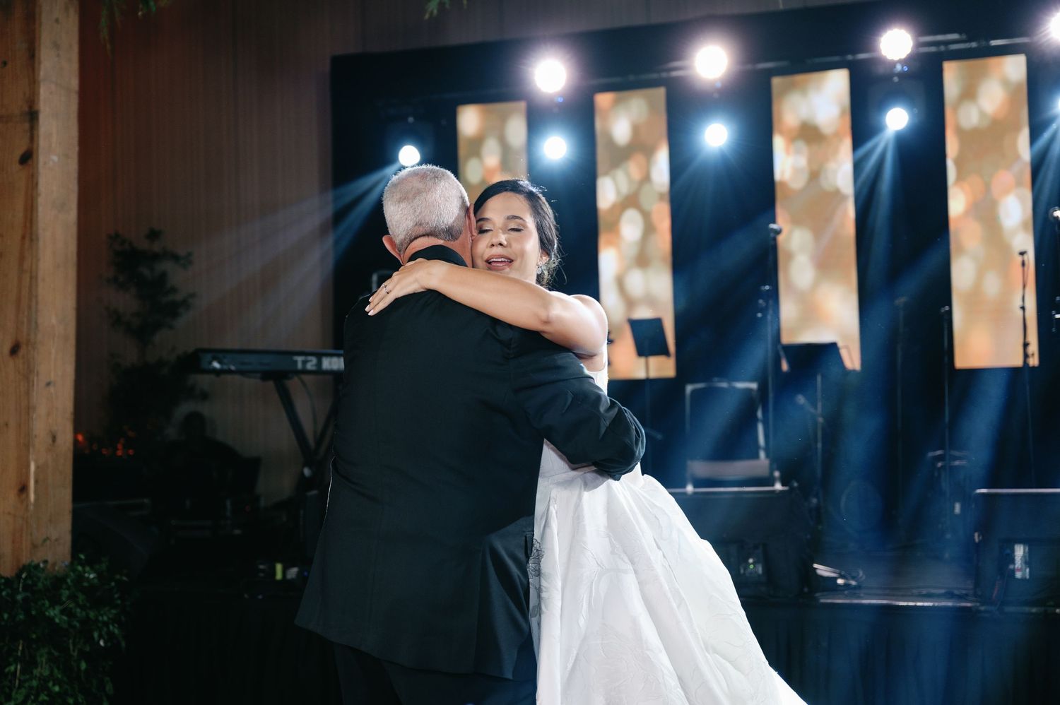A couple shares a romantic dance at an evening wedding reception with string lights glowing in the background.