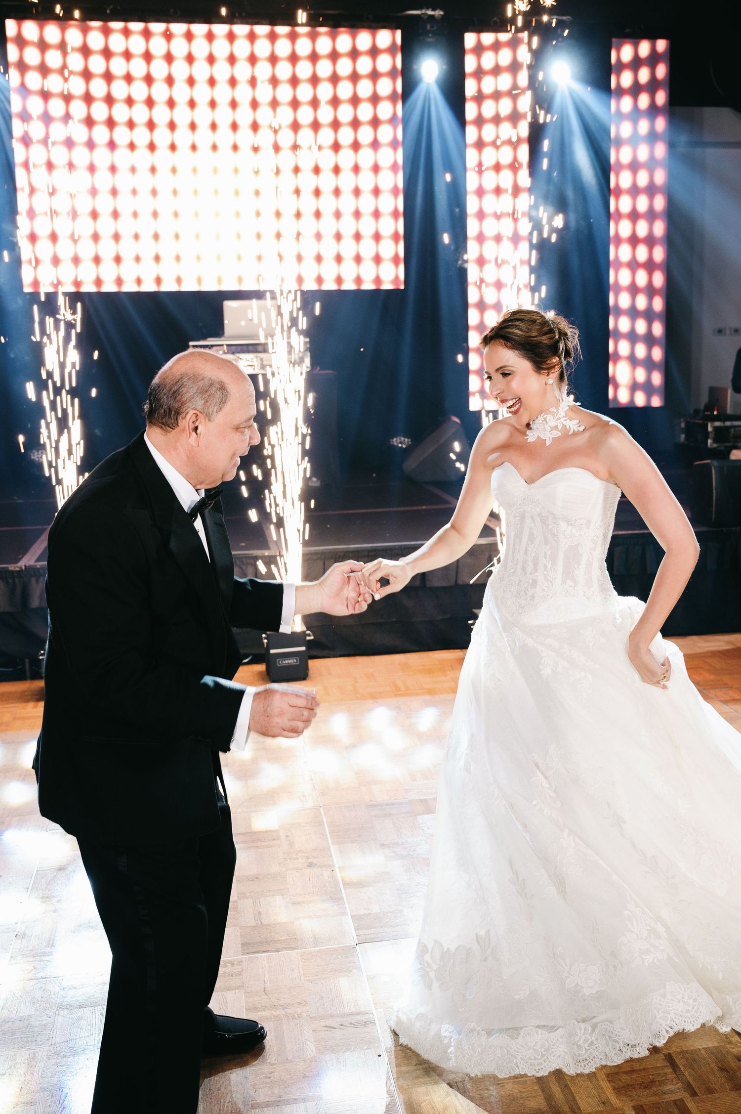 A couple spins and dances under sparkling lights with a white wedding dress flowing gracefully.