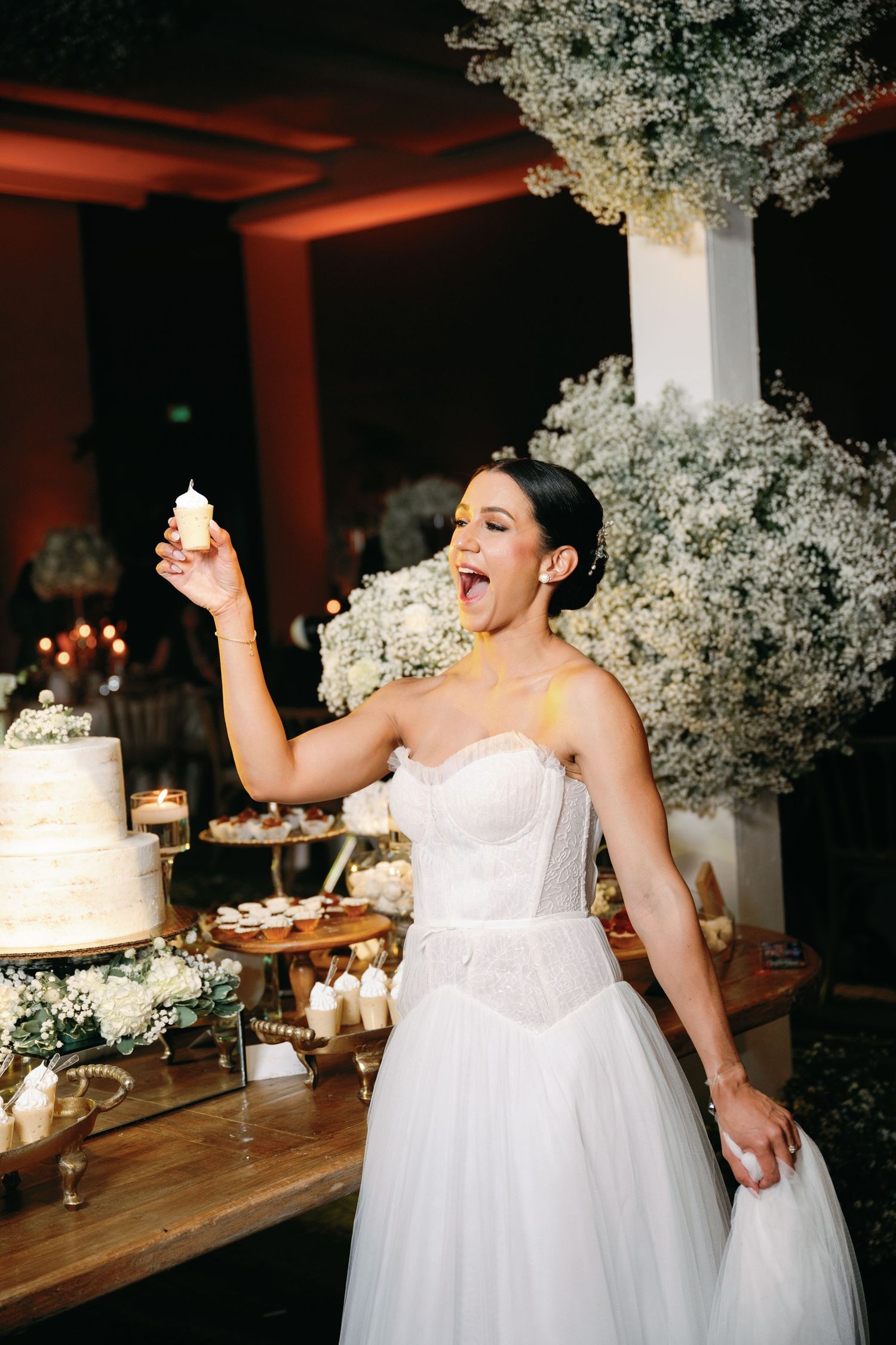 Wedding reception dessert table features an elegant white cake surrounded by floral arrangements.
