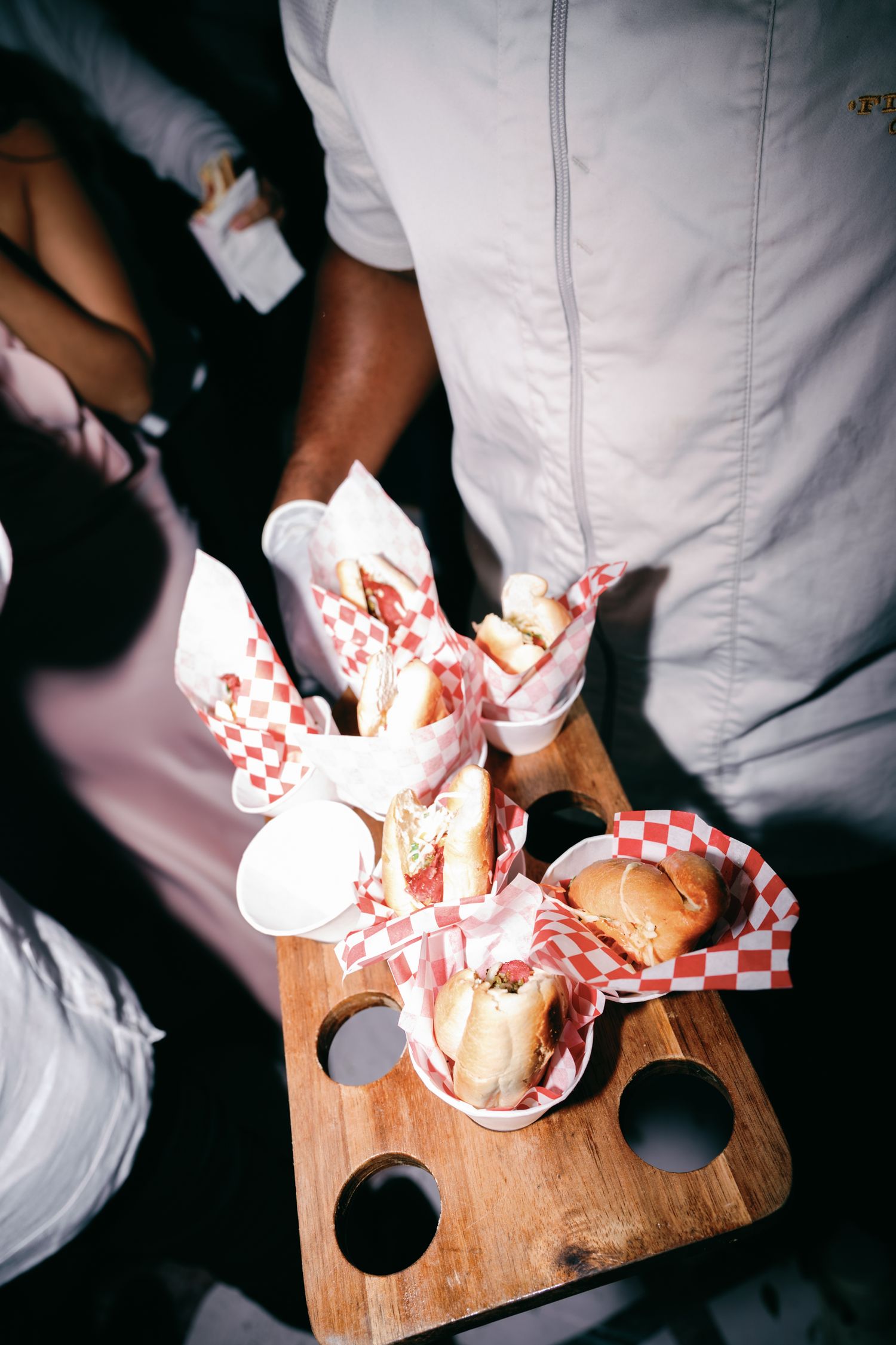 Hands in white chef coats preparing food on wooden cutting boards in a dark kitchen setting.
