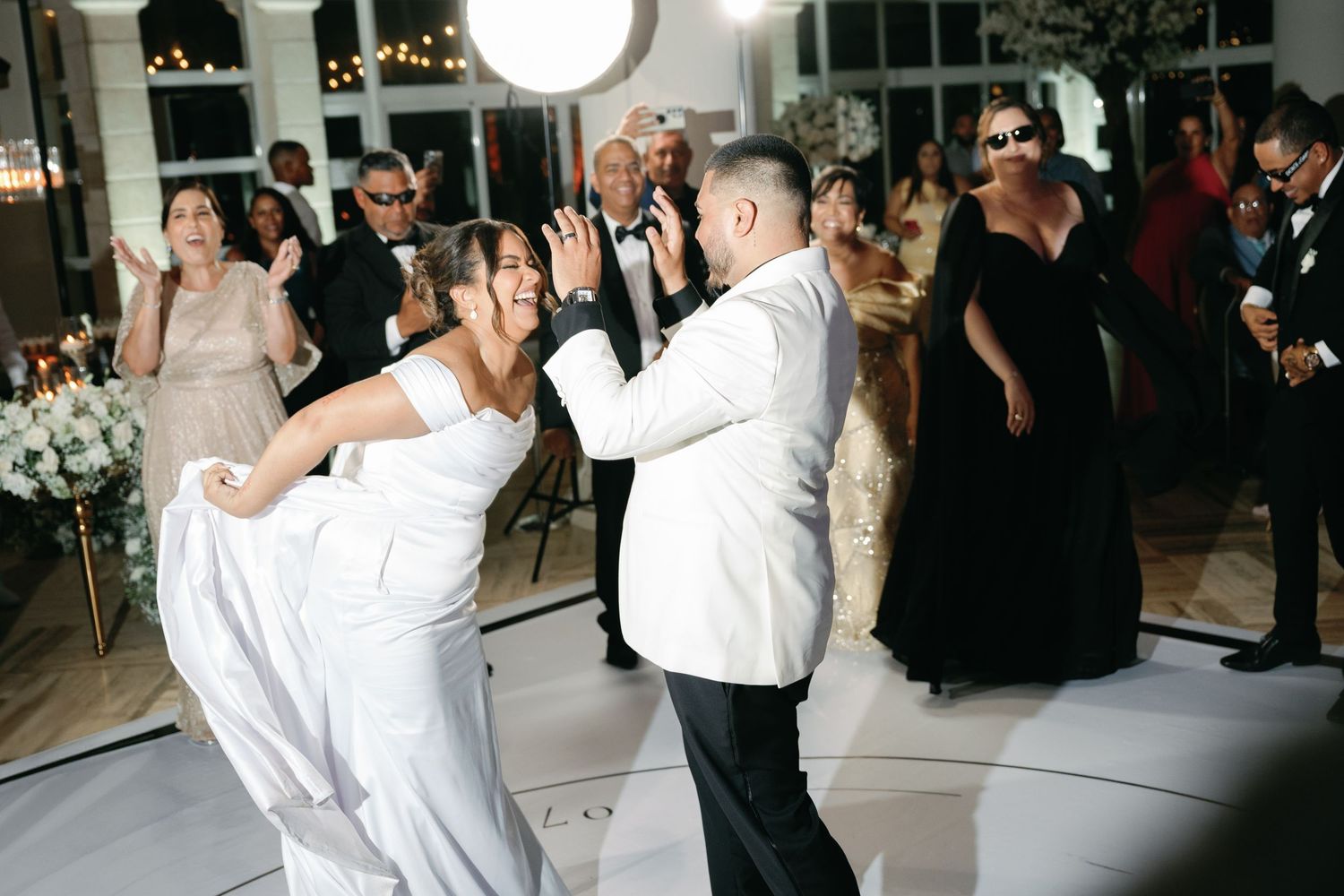 Wedding guests dance and celebrate on a dimly lit dance floor during an evening reception.