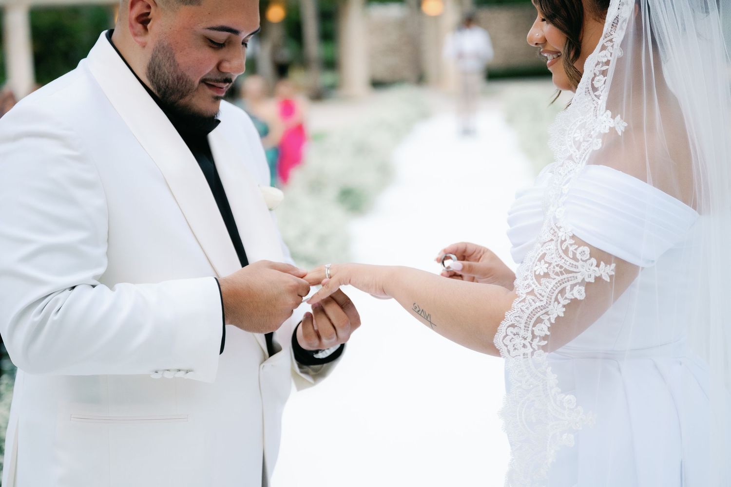 A bride and groom hold hands during their wedding ceremony while wearing traditional white wedding attire.
