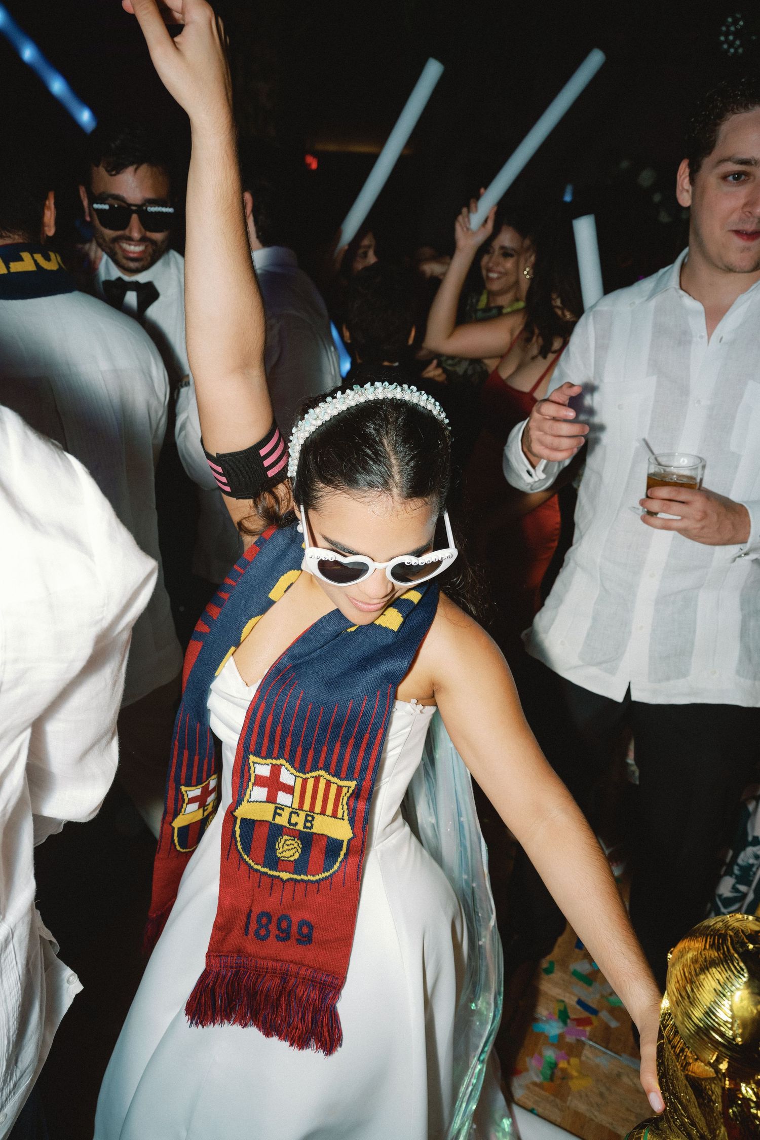 Party guests dance and celebrate while wearing FC Barcelona soccer scarves and jerseys on a dark dance floor.
