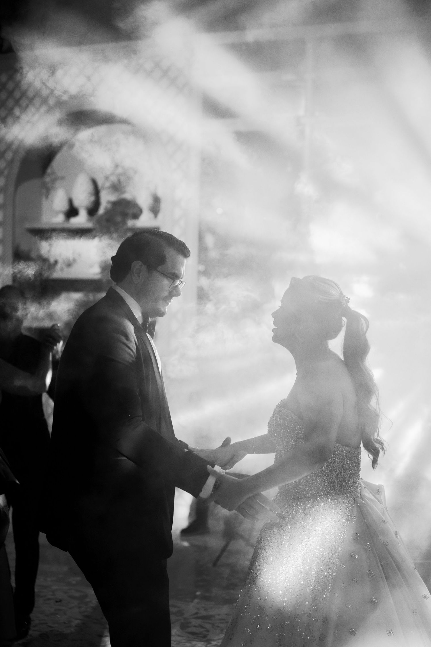 A romantic black and white wedding photo showing a couple holding hands in an ethereal, misty setting.
