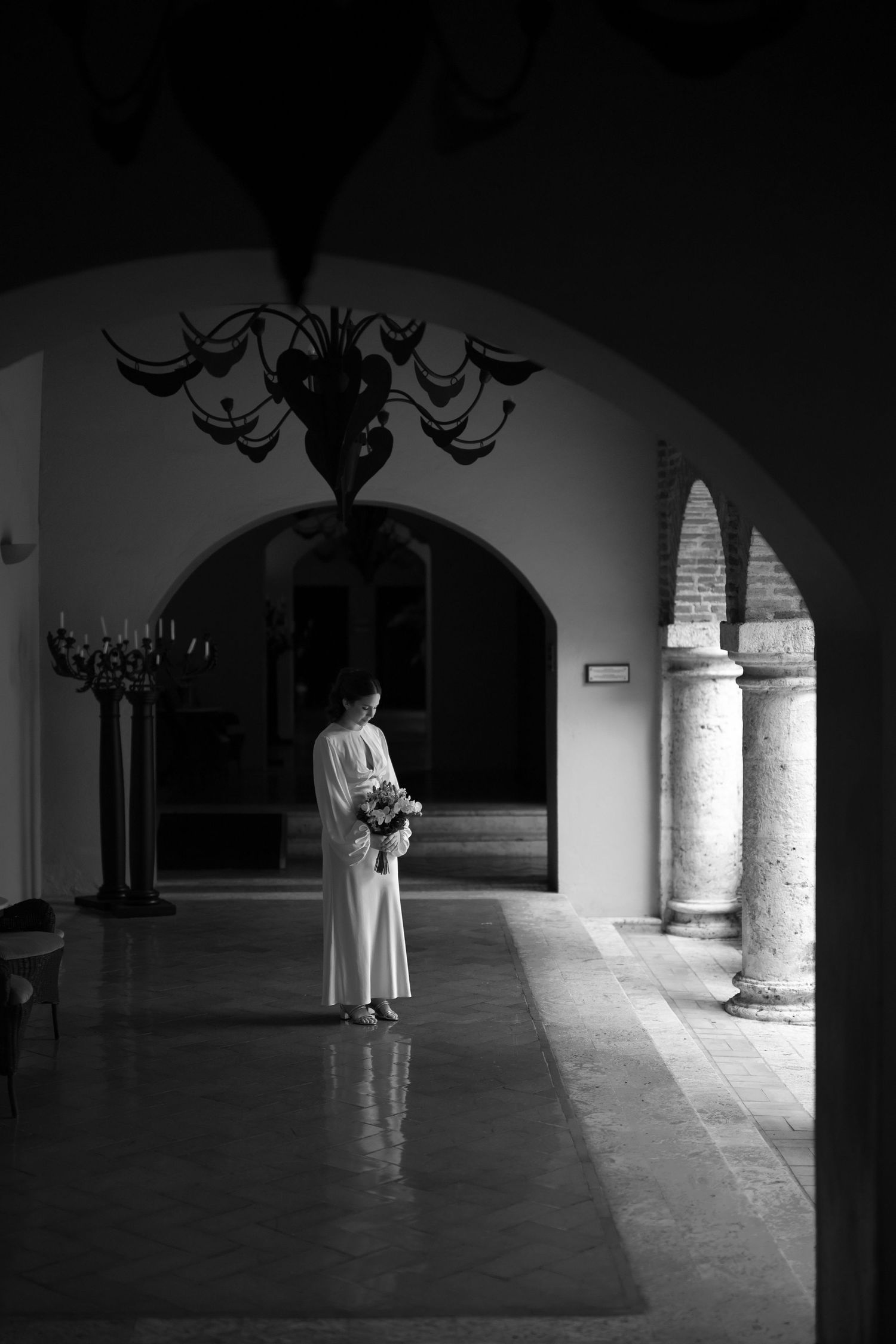 A ghostly figure in white robes stands in a dimly lit stone corridor of what appears to be a monastery or church.