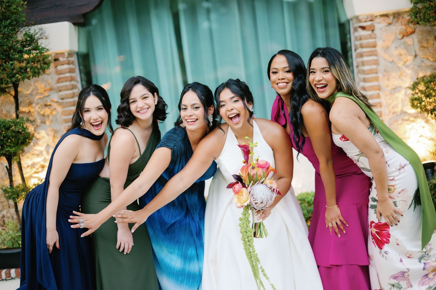 Bridesmaids in navy and magenta dresses pose together outdoors near a brick building.