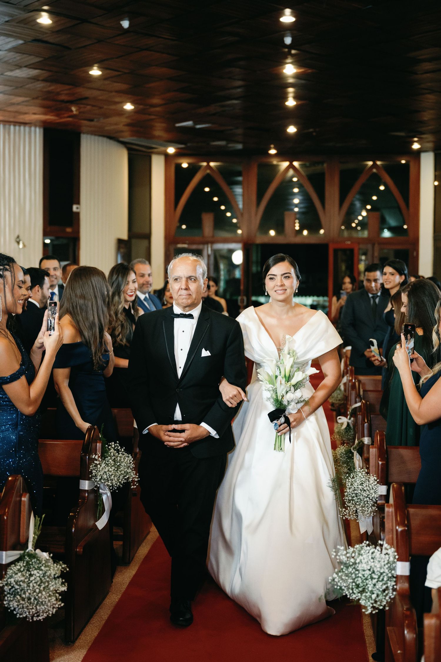 Wedding ceremony processional in an elegant venue with red carpet aisle and baby's breath floral decorations.