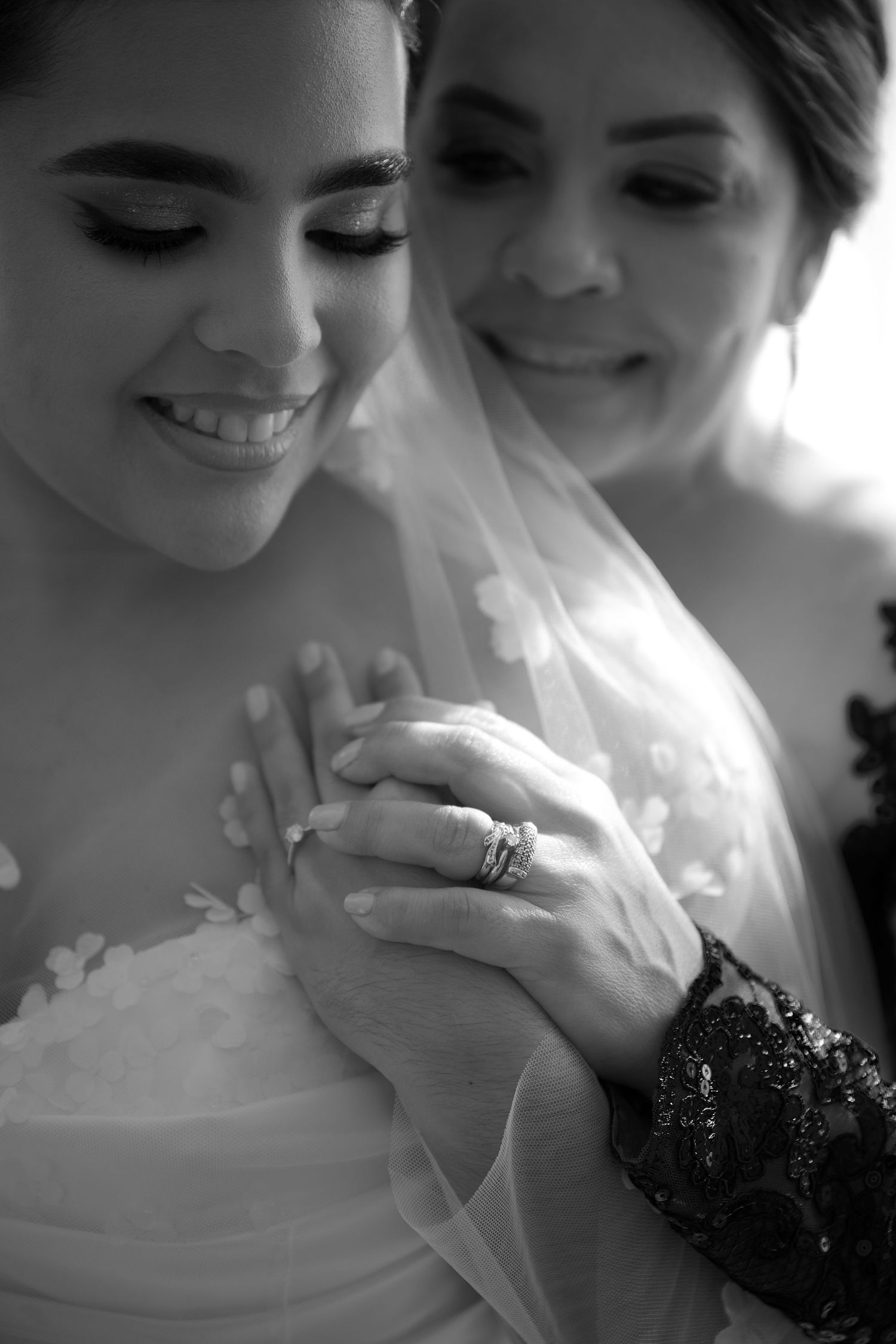 Black and white wedding photo showing bride in veil and wedding dress with engagement ring in intimate moment.