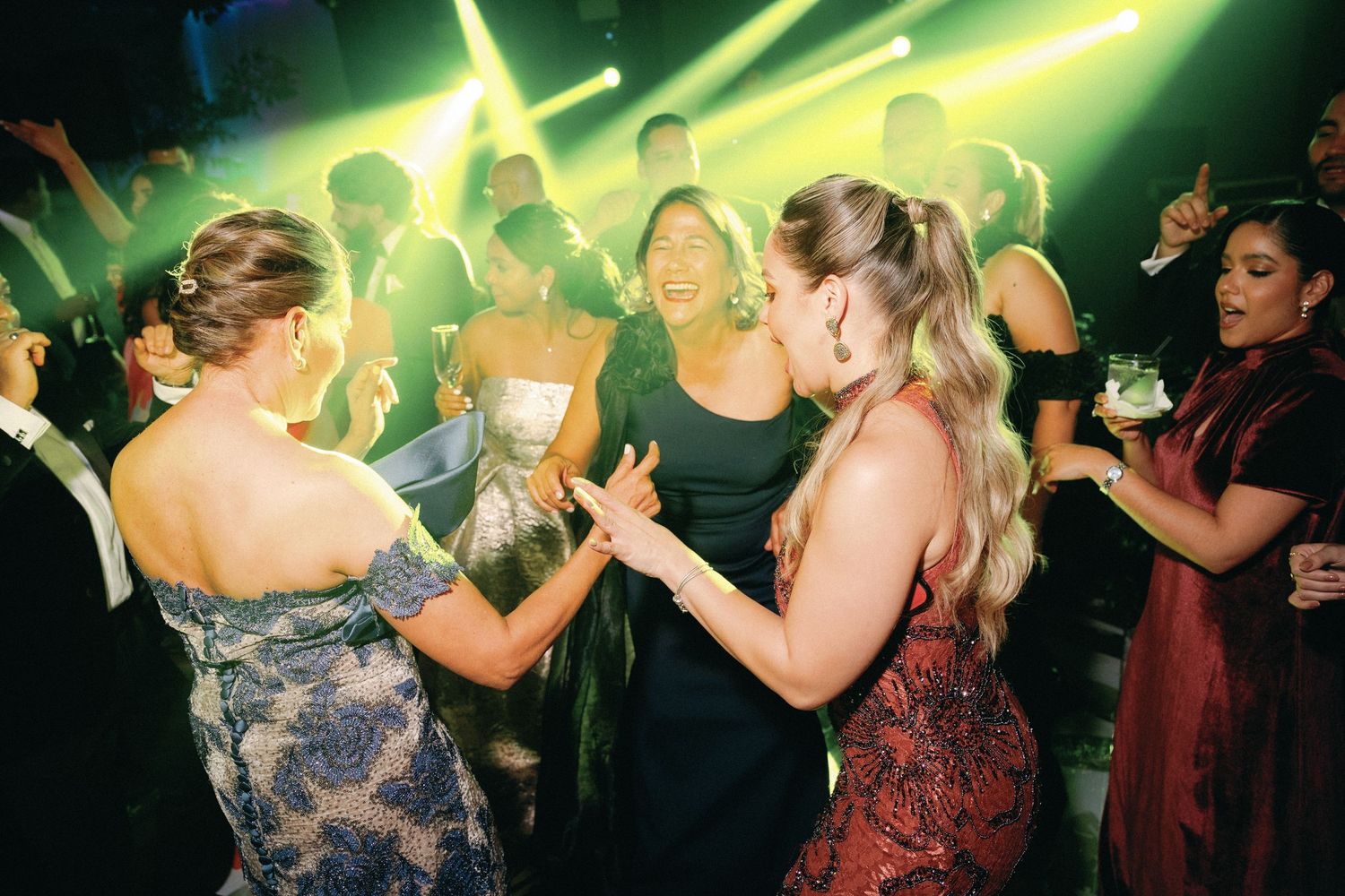 Wedding guests dancing under bright green lighting at a nightclub-style reception party.