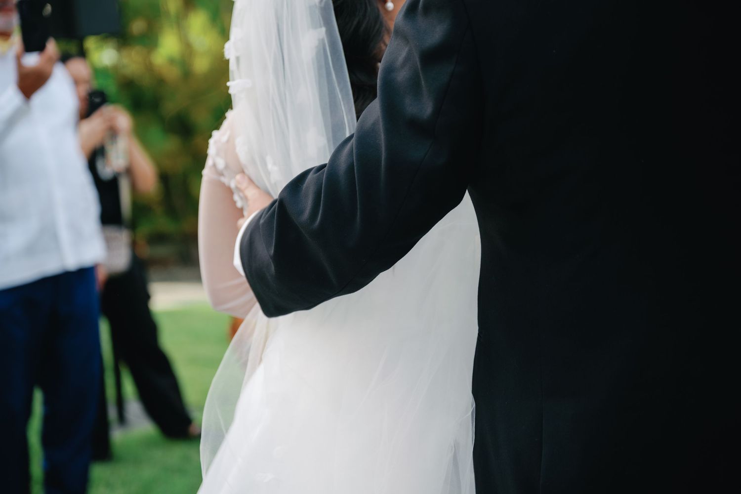 A close-up view of a bride and groom embracing during an outdoor wedding ceremony.