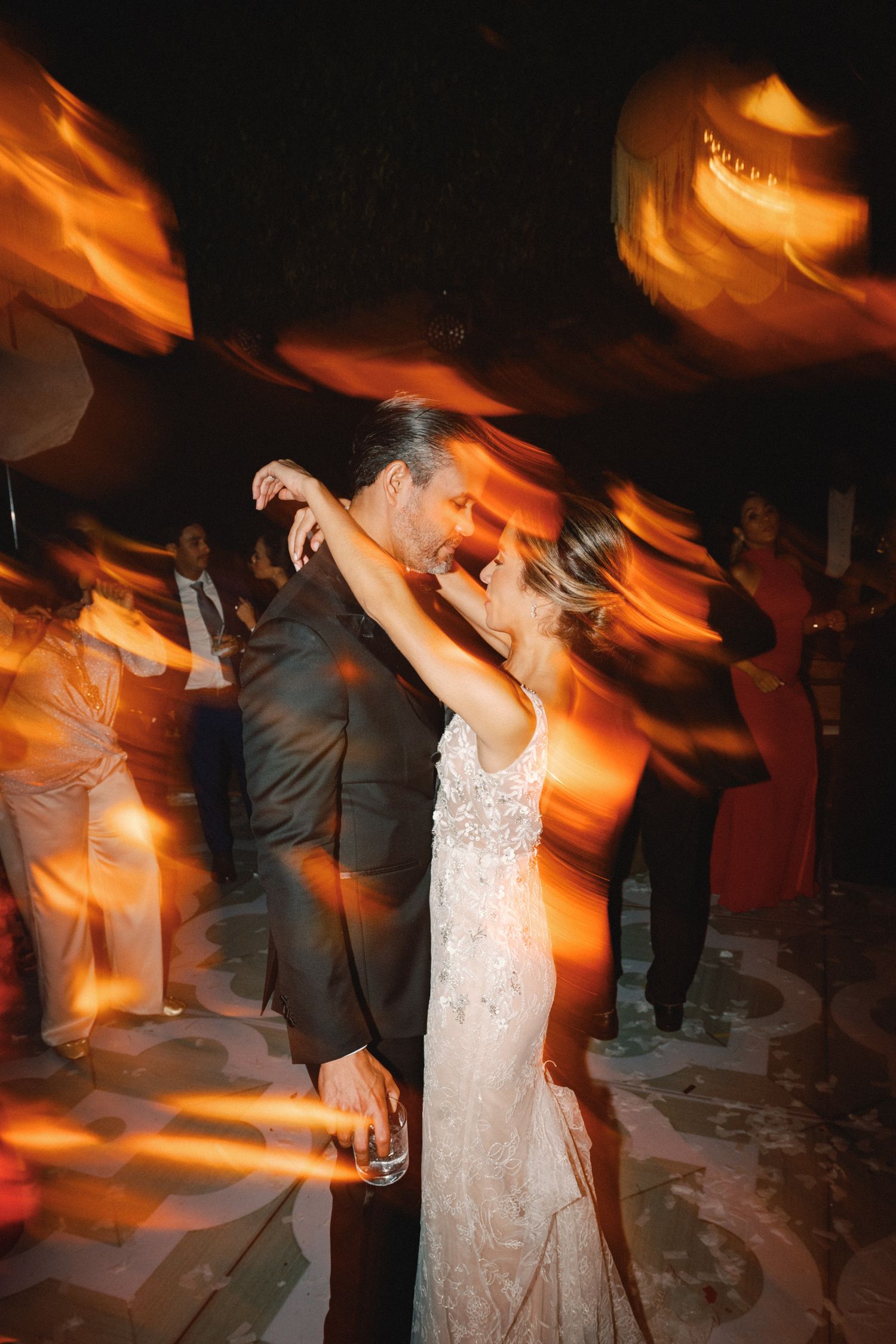 Couples dancing at a wedding reception under warm orange lighting create motion blur effects.