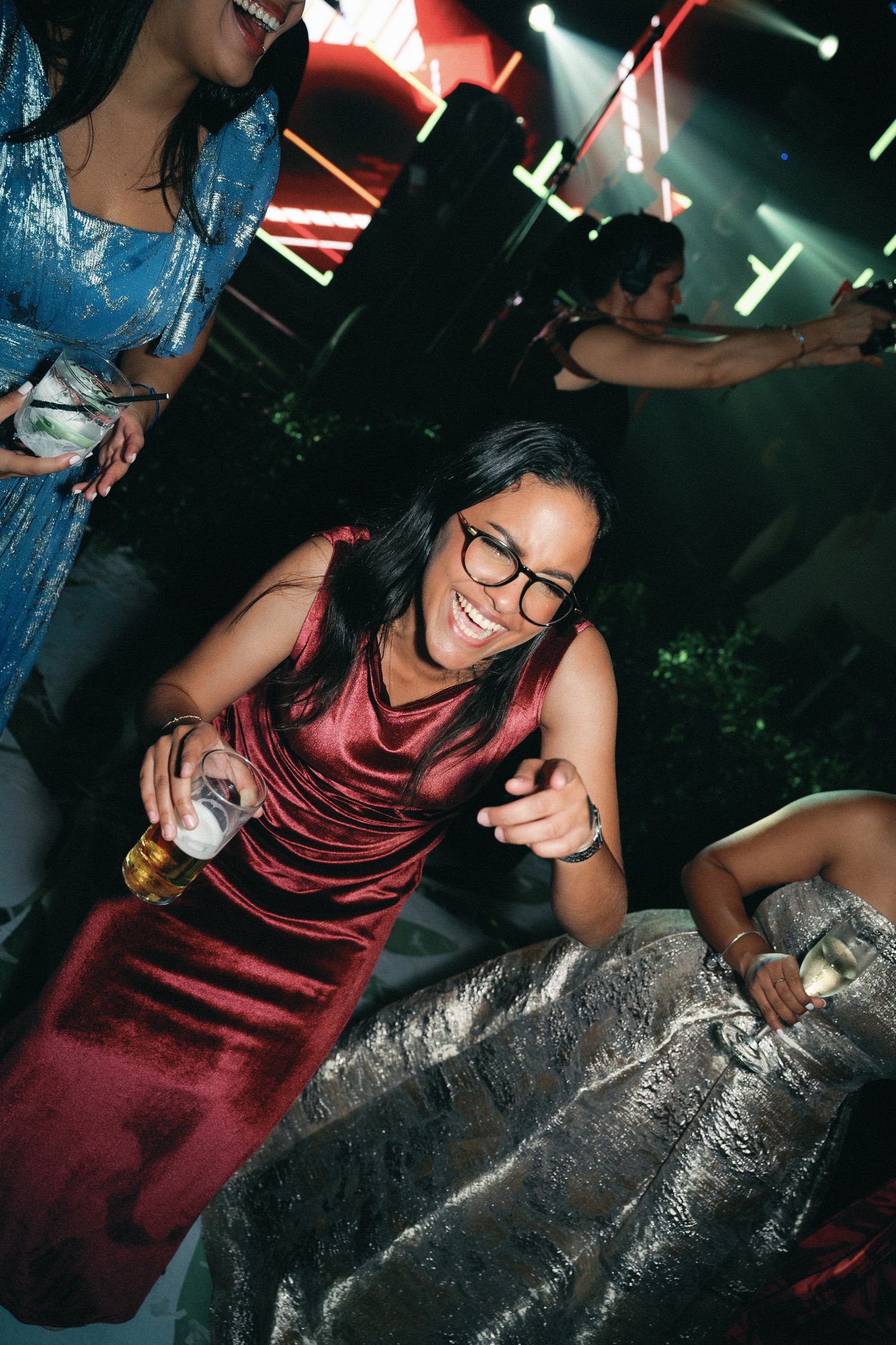 A person in a burgundy top and glasses lounges on a metallic surface at a party.