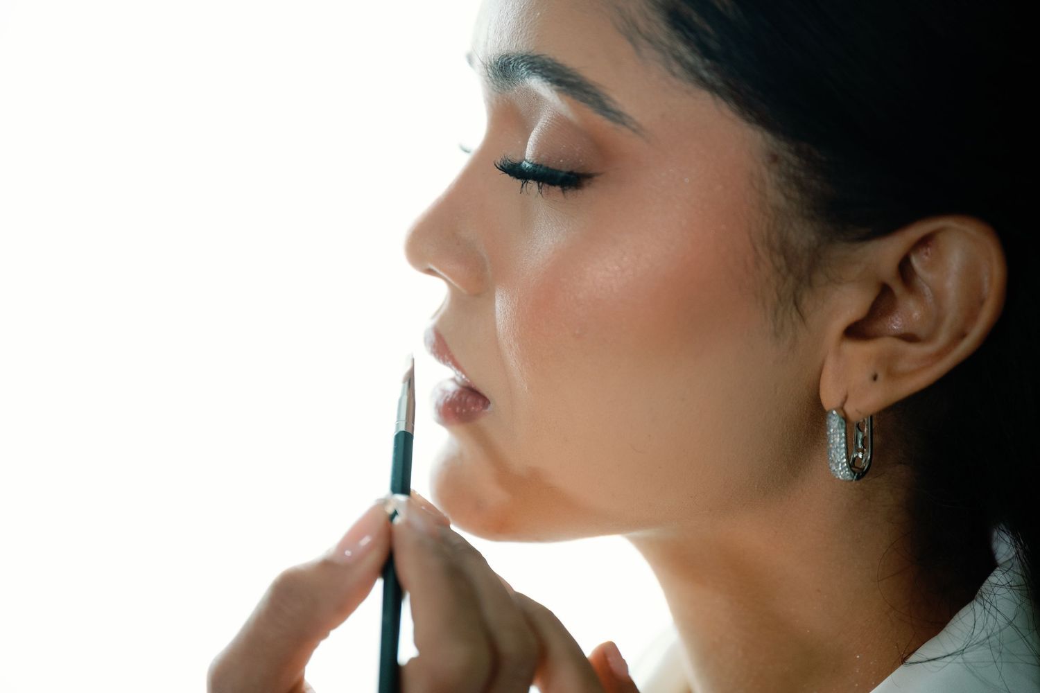Professional makeup artist applying mascara to model's eyelashes during beauty photoshoot.