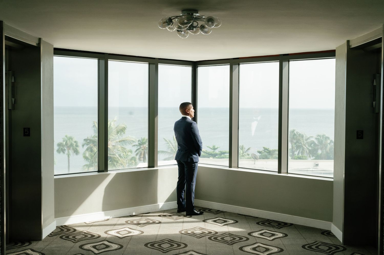 A modern apartment with floor-to-ceiling windows and a person standing in silhouette against panoramic city views.