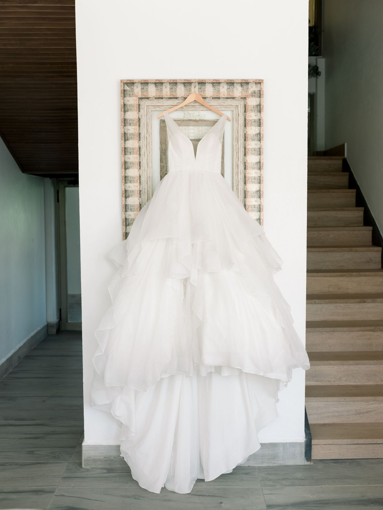 A white wedding dress displayed in sequence against a light interior wall with stairs visible in the background.