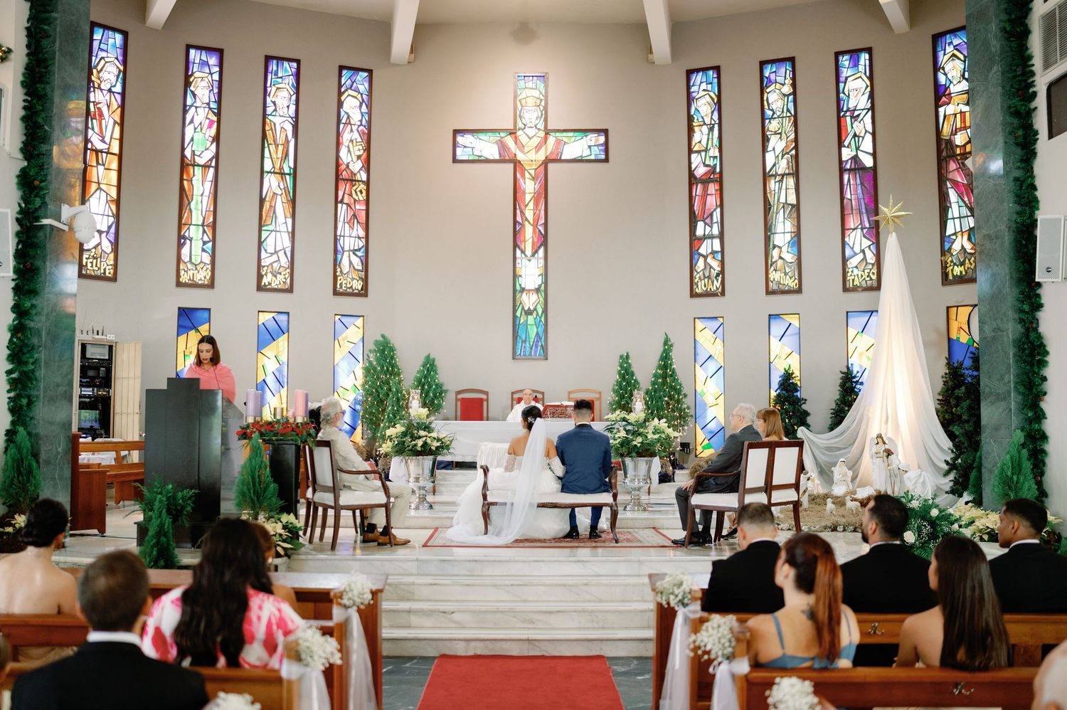 A panoramic view of a church interior with stained glass windows and decorated columns during a wedding ceremony.