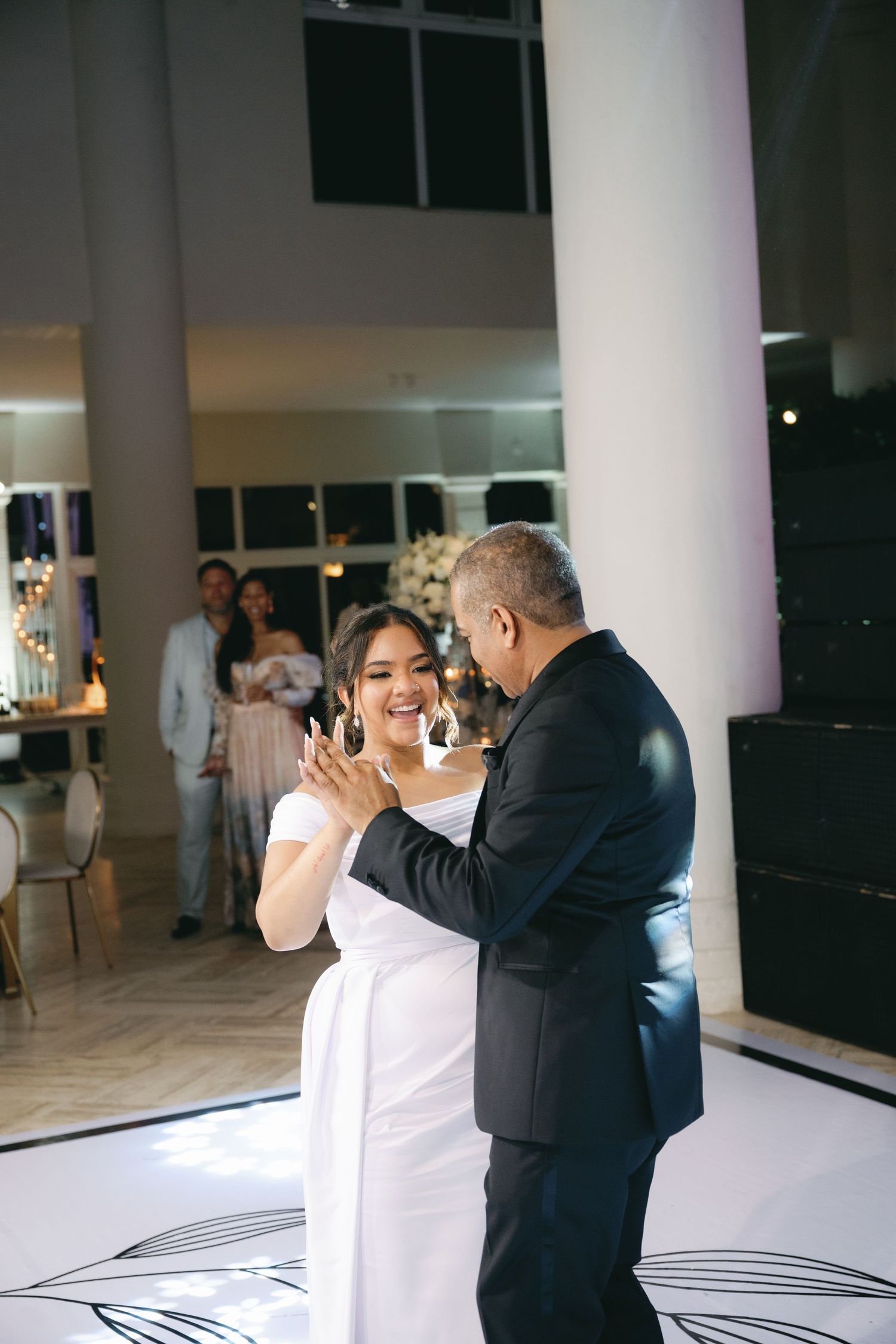 A couple dancing together at their wedding reception in an elegant white venue with tall columns.
