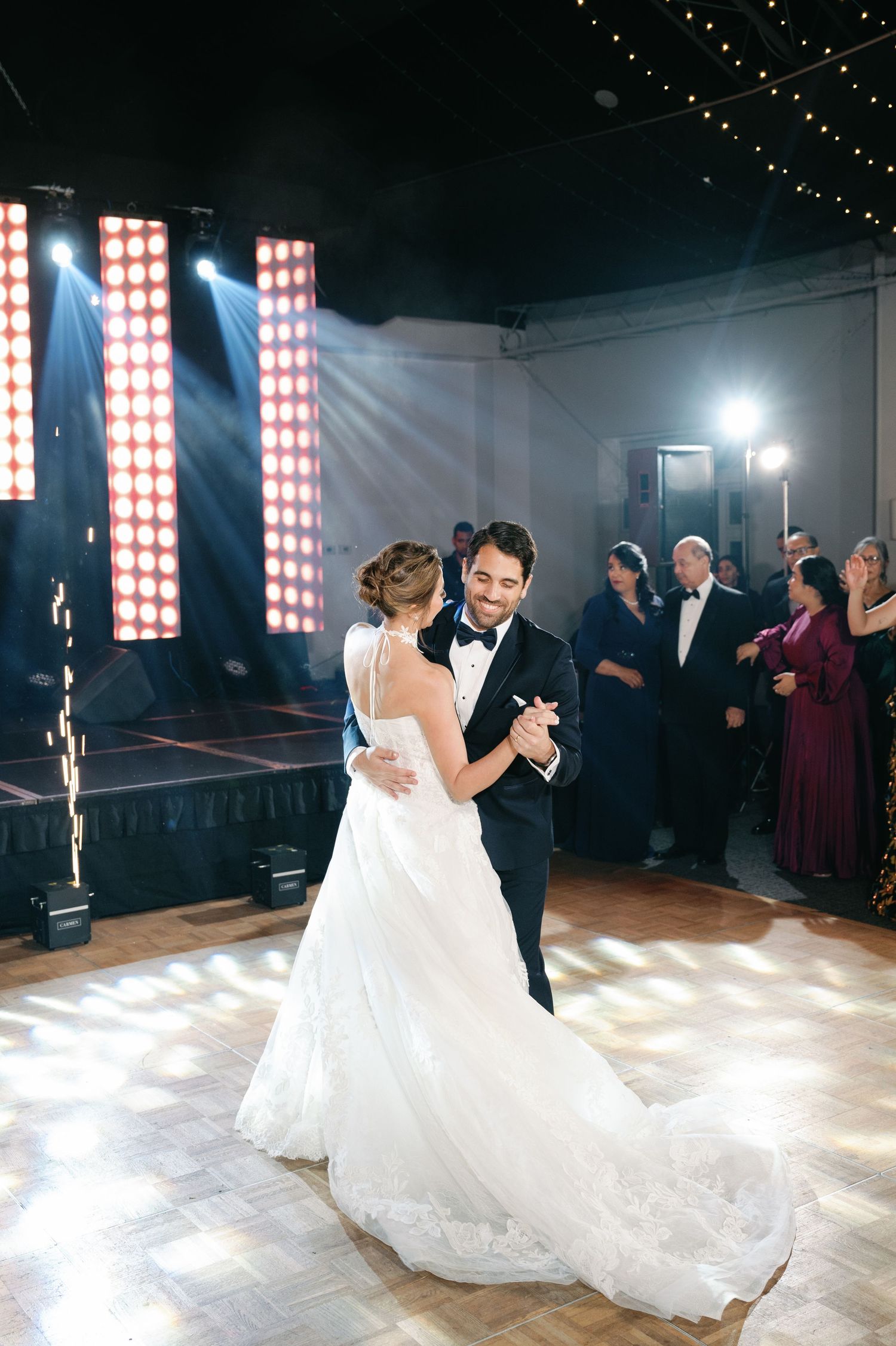 A couple shares their first dance at a wedding reception with dramatic lighting and a beautiful white gown.