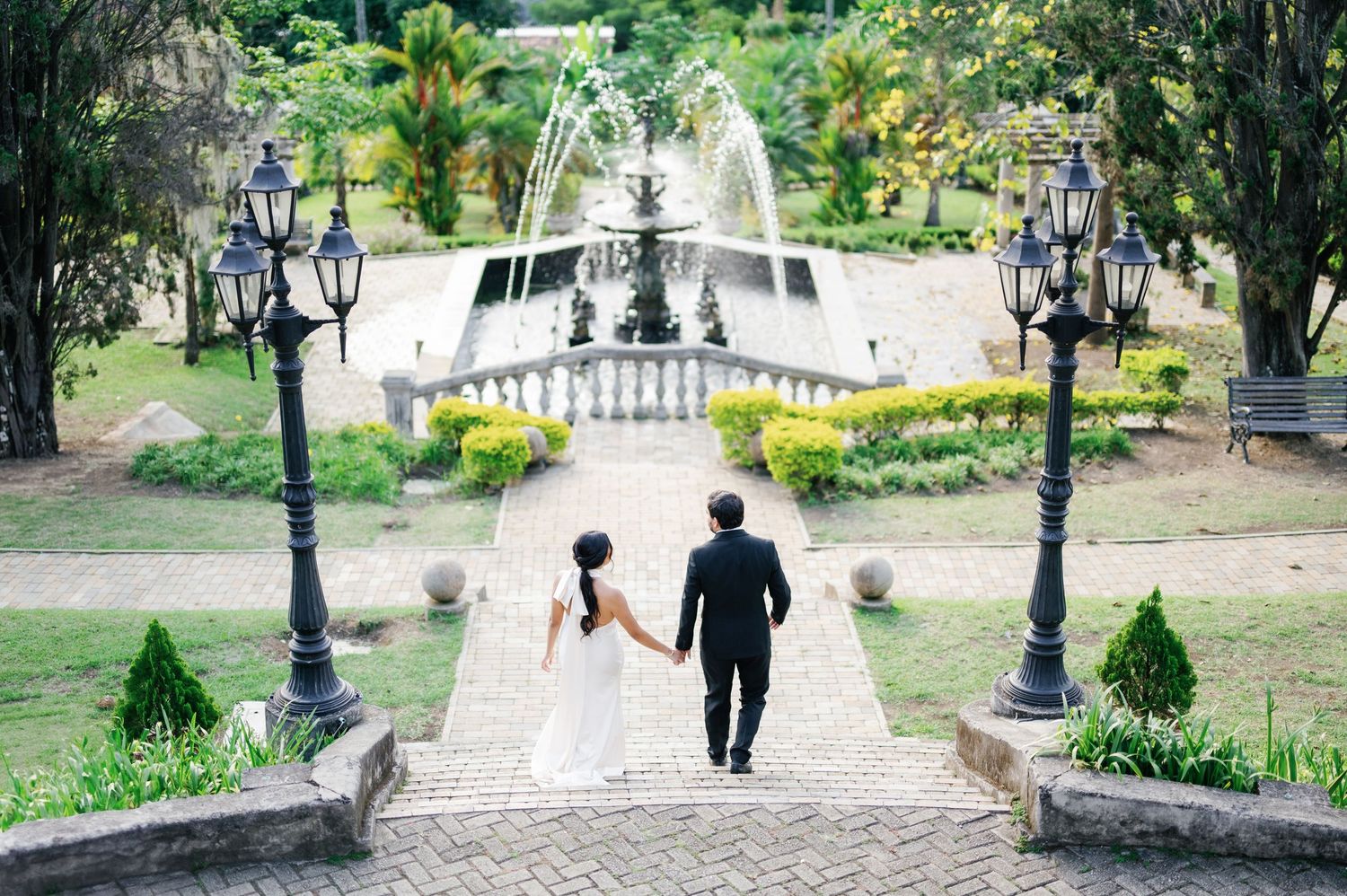A couple walking down stone steps surrounded by vintage lampposts and a cascading fountain.