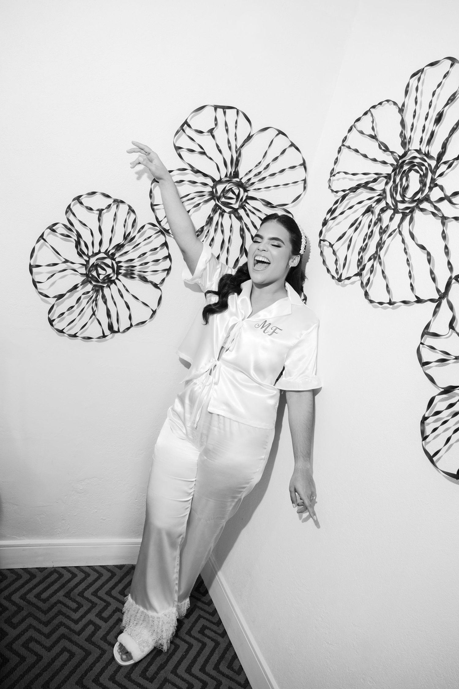 A series of four black and white photos showing joyful dancing movements against a wall decorated with floral designs.