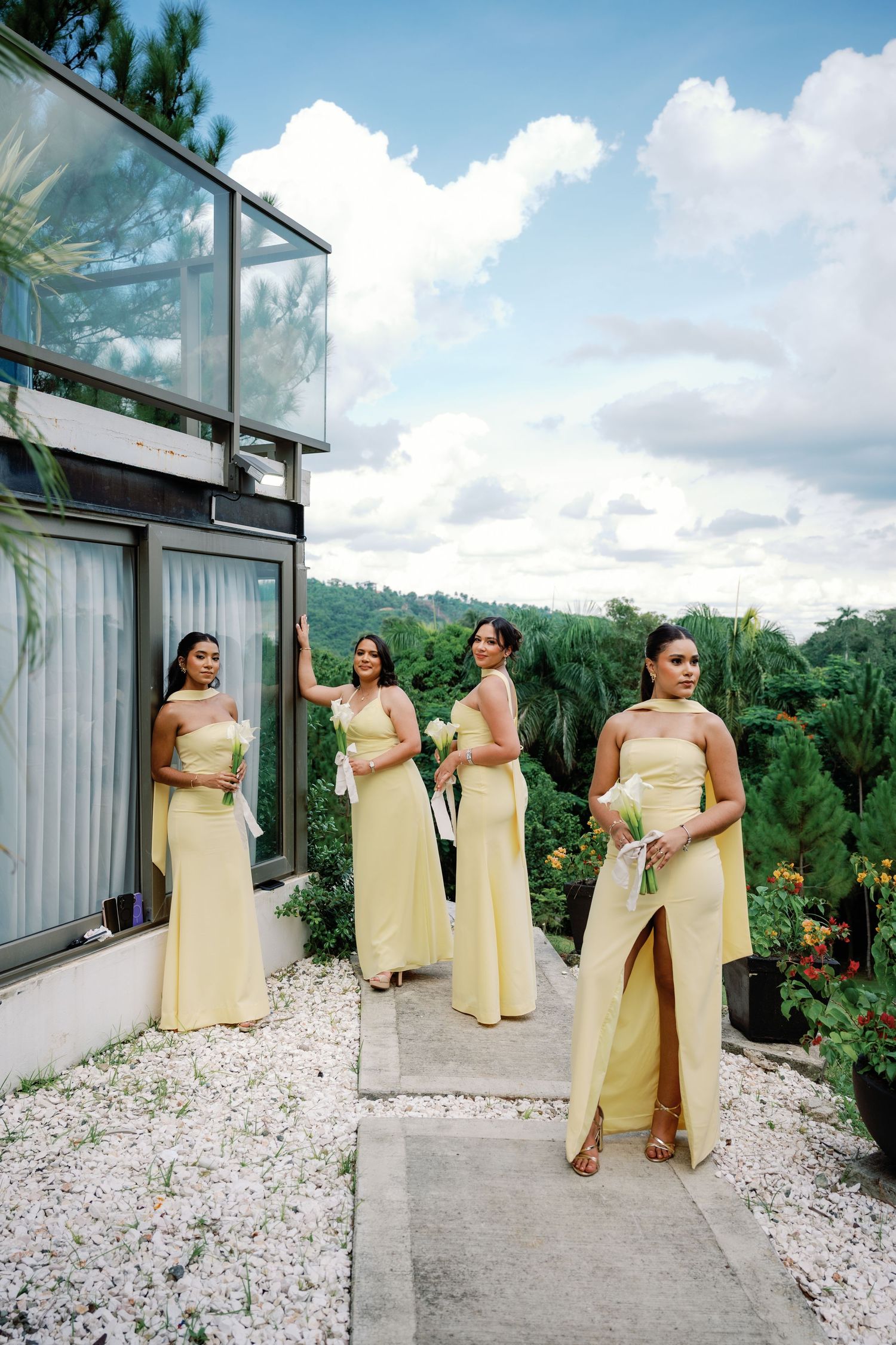 Bridesmaids in pale yellow dresses pose together on a modern terrace with mountain views.