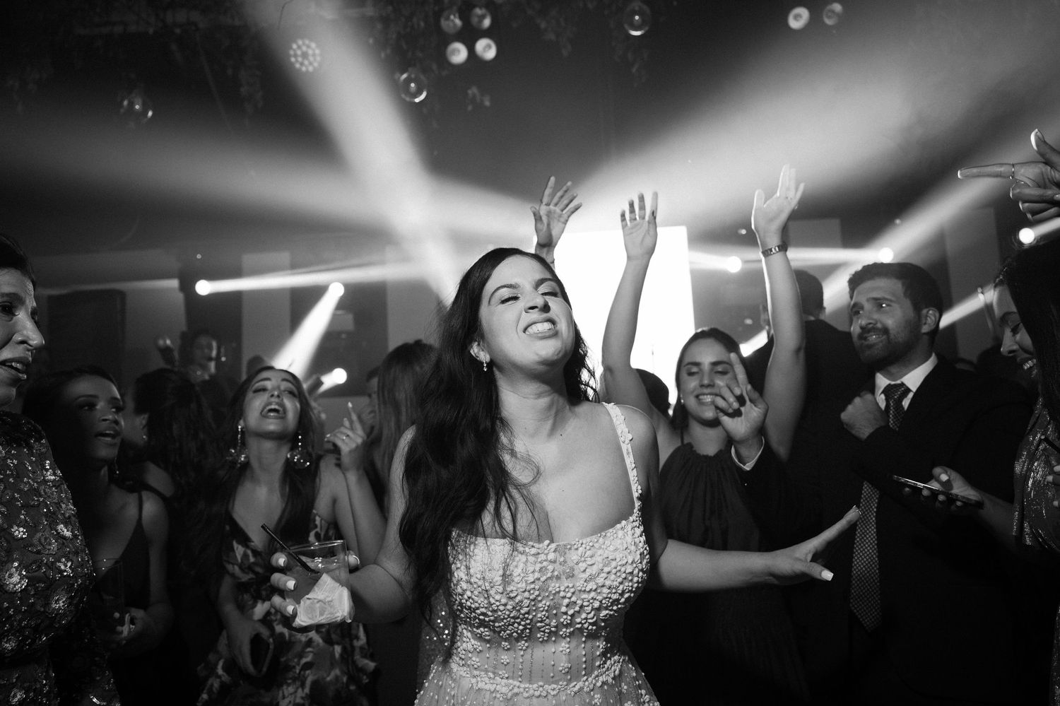 Black and white photo of people dancing and celebrating at a party with dramatic spotlights overhead.