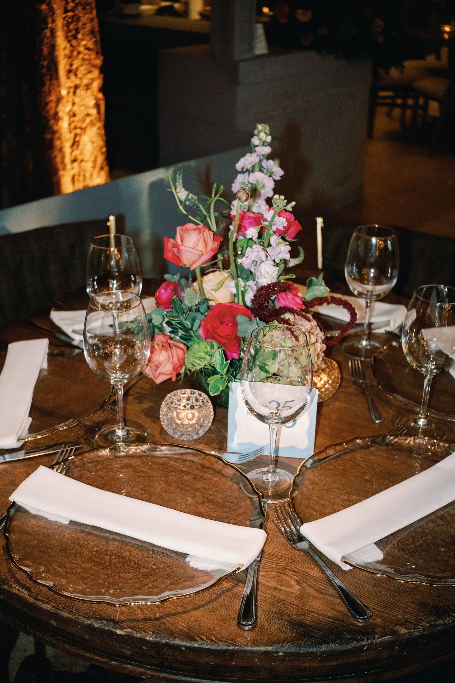 Elegant wedding reception table settings with pink floral centerpieces and wine glasses on rustic wooden tables.