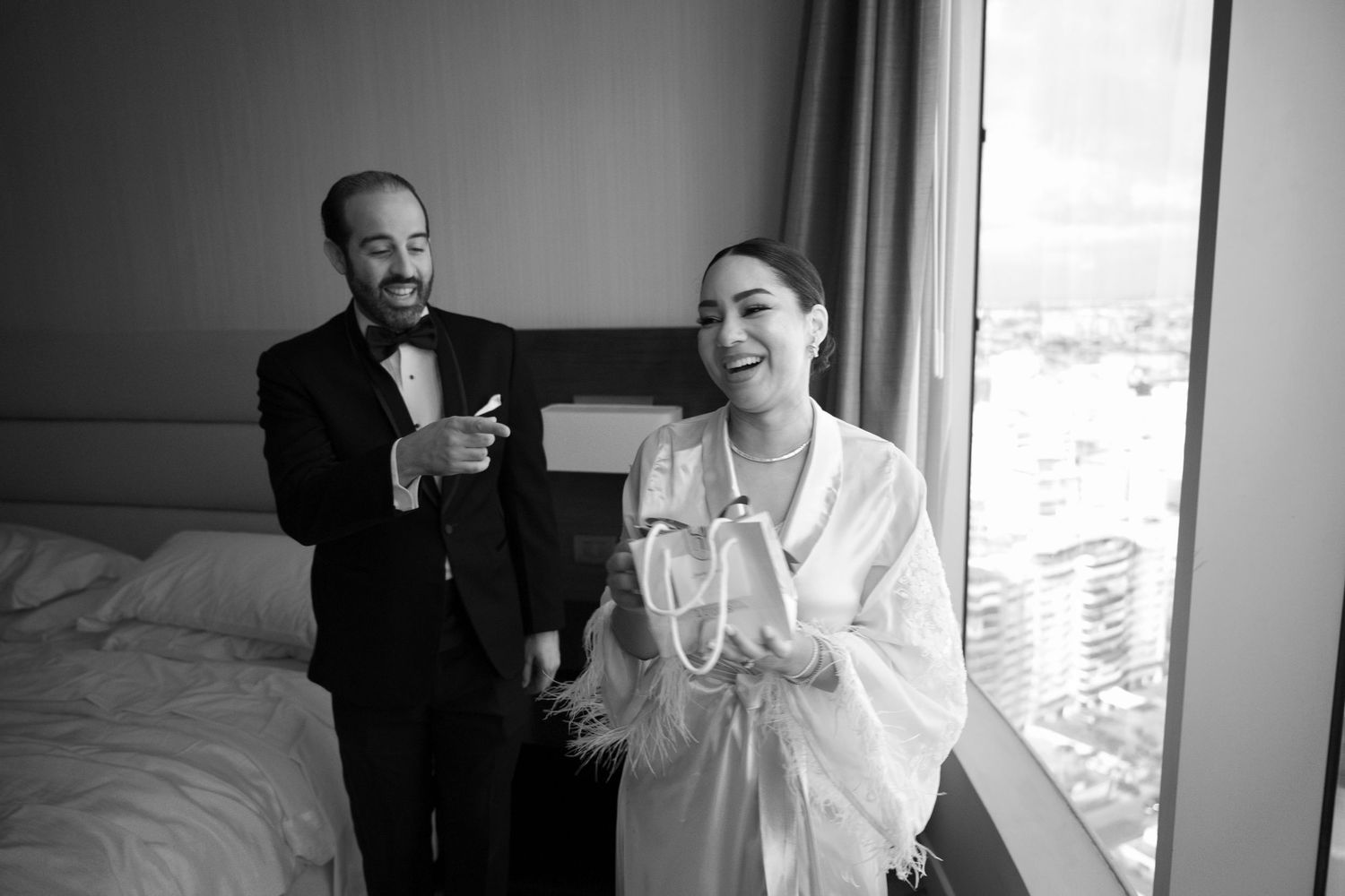 A black and white candid photo of two people in a hotel room getting ready for a formal event.