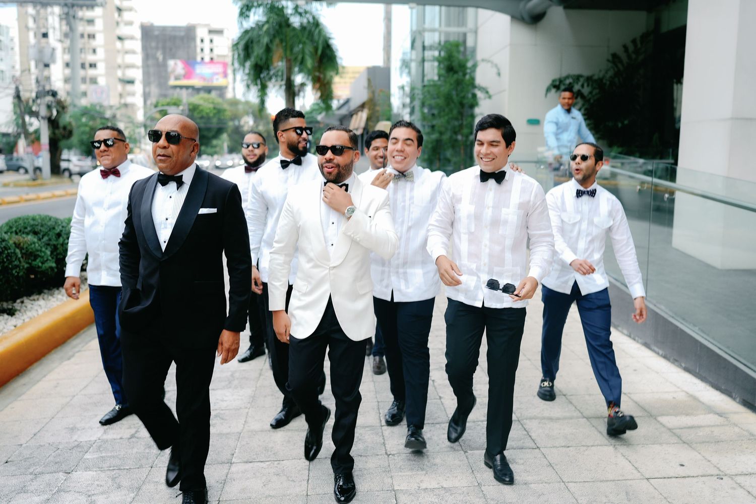 Groomsmen in formal attire walk together down a city street during a wedding celebration.