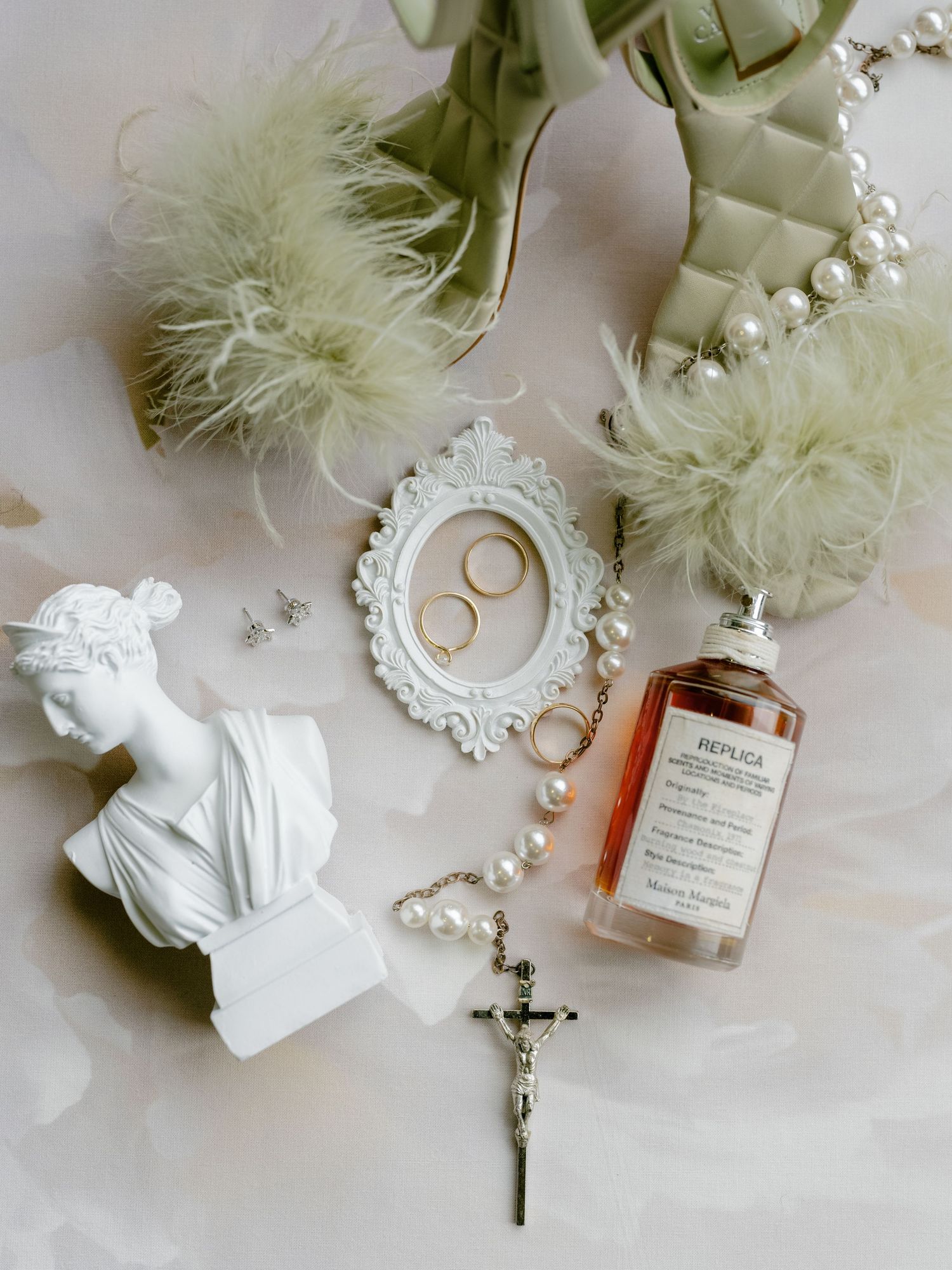 Wedding details flatlay with rings, cross, and delicate white decorative elements.