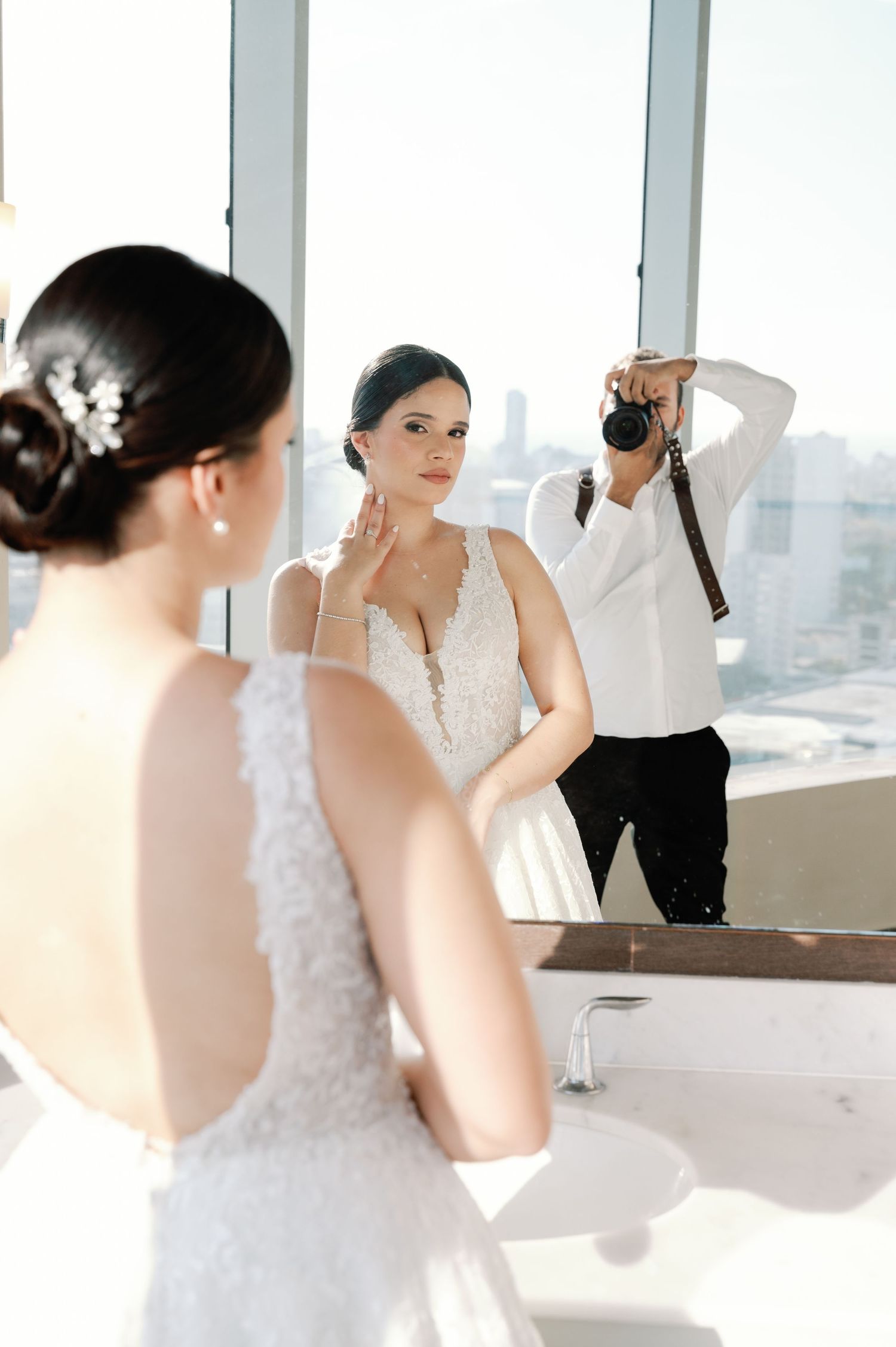 Bride in white lace dress looking at her reflection in a modern high-rise window.