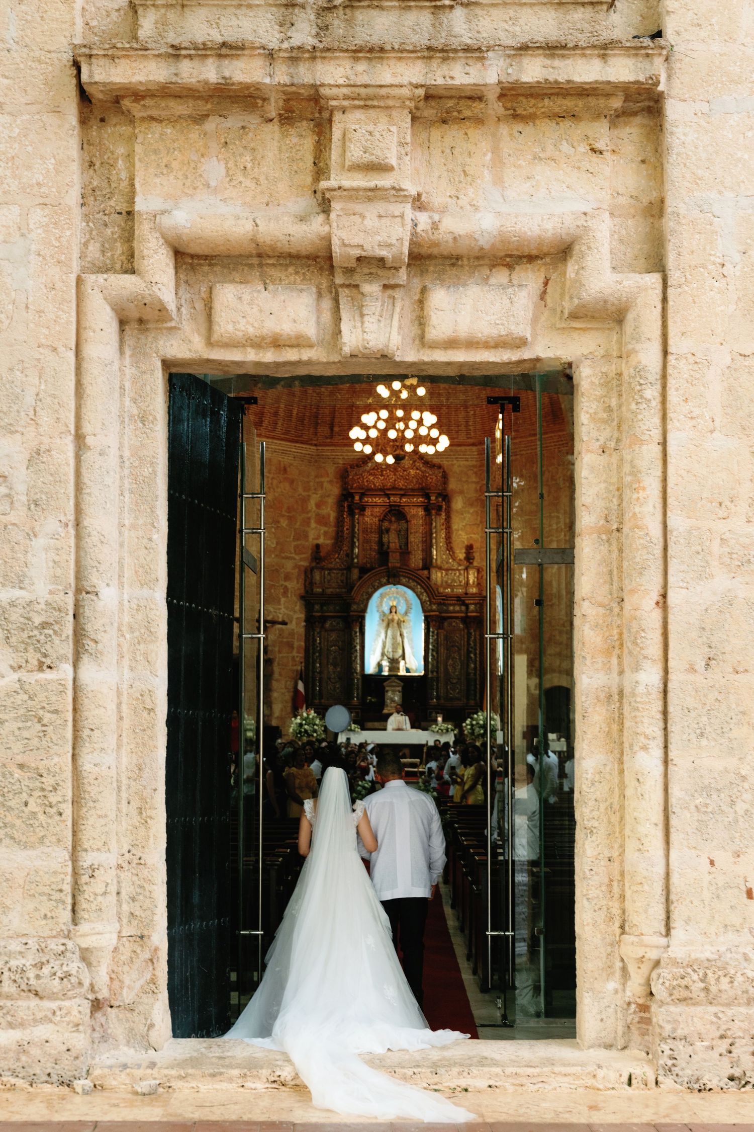 Stone church entrance framed with elegant architecture and illuminated interior showing wedding preparations.