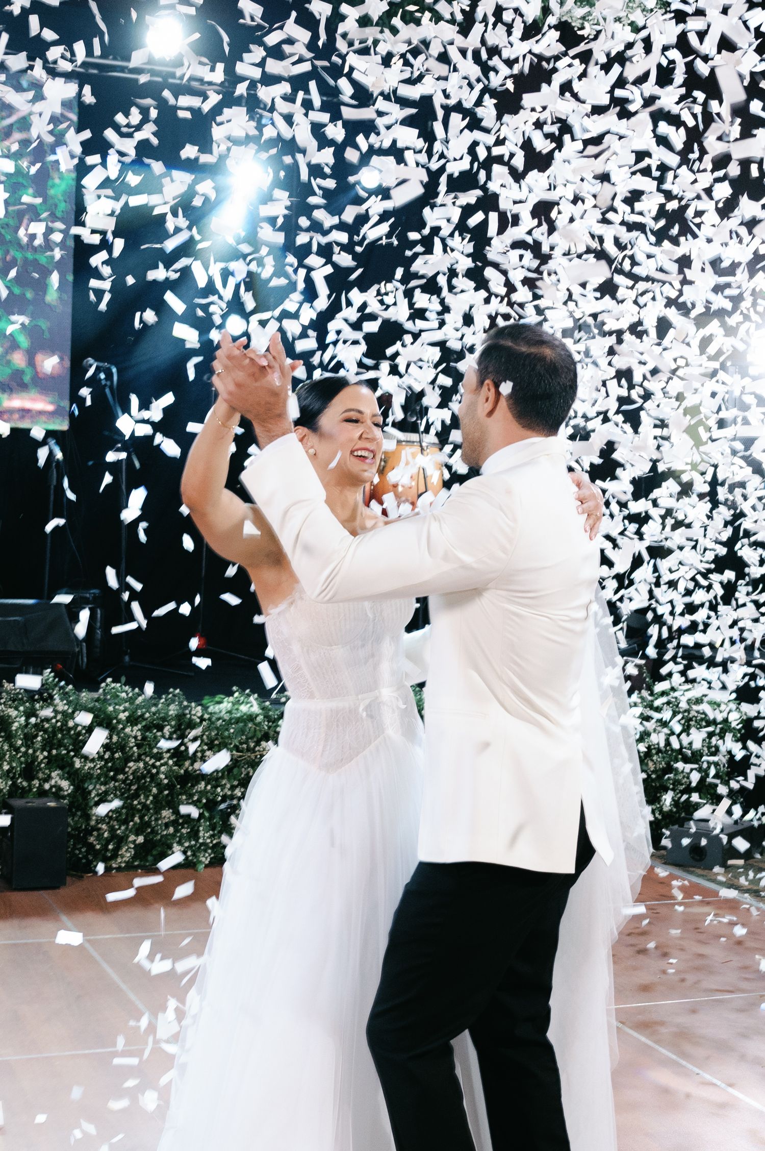A couple shares their first dance as newlyweds while white confetti falls around them in a romantic celebration.
