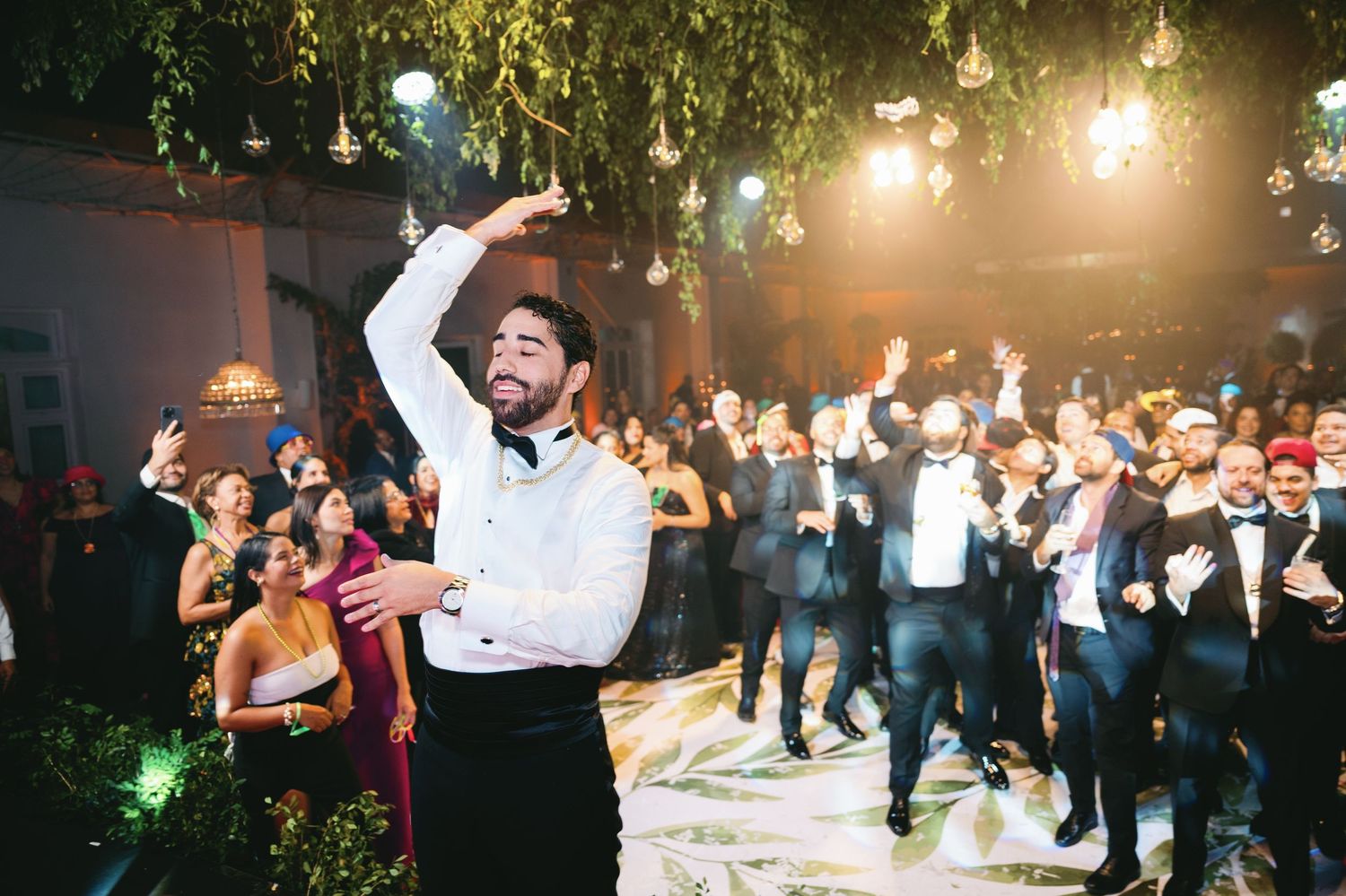 Energetic partygoer in white dress shirt dances enthusiastically among a cheering crowd at a formal event.