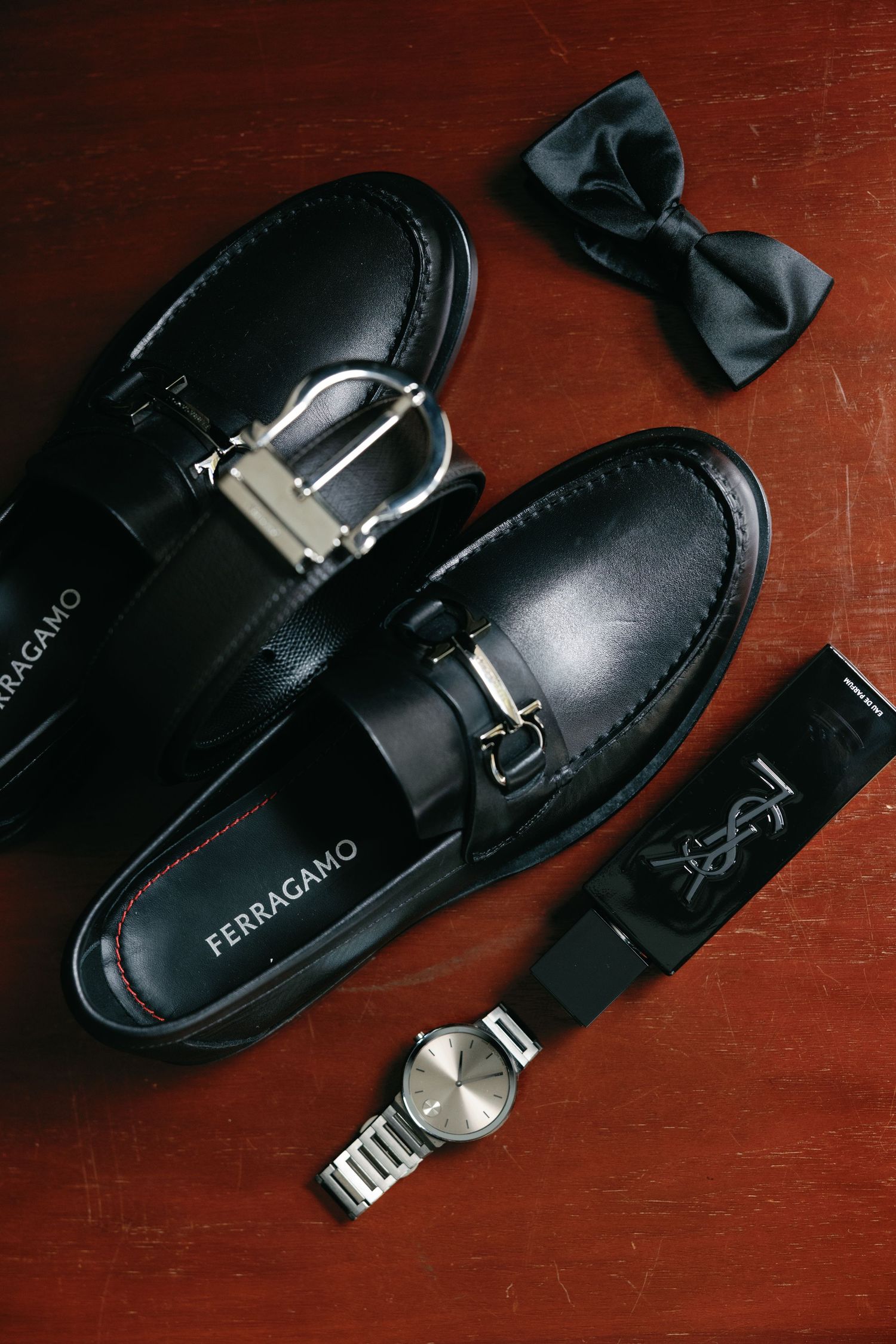 Black leather dress shoes and accessories arranged on a dark wooden surface.